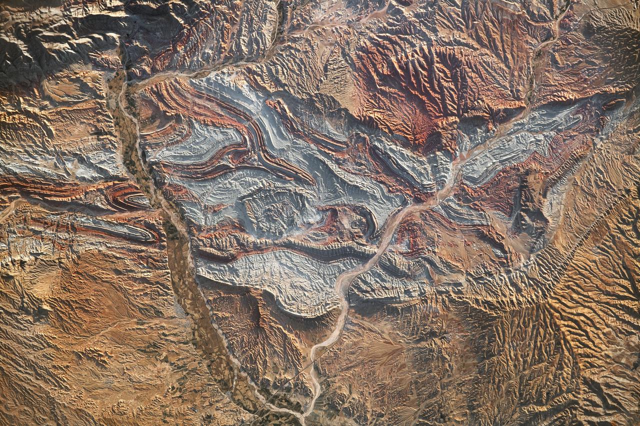 iss069-e-089946_lrg (09/19/2023)  --- An astronaut aboard the International Space Station took this photograph of the rugged landscape of the Aladaghlar Mountains in northwestern Iran. Ridges cast shadows in the valleys and other low elevation areas, creating a three-dimensional appearance. Human alterations to the landscape are most evident in riverbeds, where the even topography is easier to build on and navigate.  Natural processes over millions of years have folded rock layers of various compositions and colors into the curved patterns seen here. These folds are produced by tectonic forces operating along the convergent plate boundary of the Arabia and Eurasia plates. The convergence of these tectonic plates causes uplift, folding, and deformation of the colorful rock layers, and subsequent erosion exposes them.  On the left side of this photo, the Qezel Ozan River, a major river in northern Iran, cuts across the landscape. Agricultural fields are visible along the riverbanks tucked between the mountains. The Qezel Ozan also intersects the Zanjan-Tabriz freeway (Freeway 2), a major thoroughfare built on a dried riverbed connecting the cities of Tehran and Tabriz.  Astronaut photograph ISS069-E-89946 was acquired on September 19, 2023, with a Nikon D5 digital camera using a focal length of 400 millimeters. The image was provided by the ISS Crew Earth Observations Facility and the Earth Science and Remote Sensing Unit at Johnson Space Center. The image was taken by a member of the Expedition 69 crew. It has been cropped and enhanced to improve contrast, and lens artifacts have been removed. The International Space Station Program supports the laboratory as part of the ISS National Lab to help astronauts take pictures of Earth that will be of the greatest value to scientists and the public and to make those images freely available on the Internet. Additional images taken by astronauts and cosmonauts can be viewed at the NASA/JSC Gateway to Astronaut Photography of Earth. Caption by Sara Schmidt, GeoControl Systems, JETS II Contract at NASA-JSC and Andrea Wenzel, Jacobs-JETS II Contract at NASA-JSC.