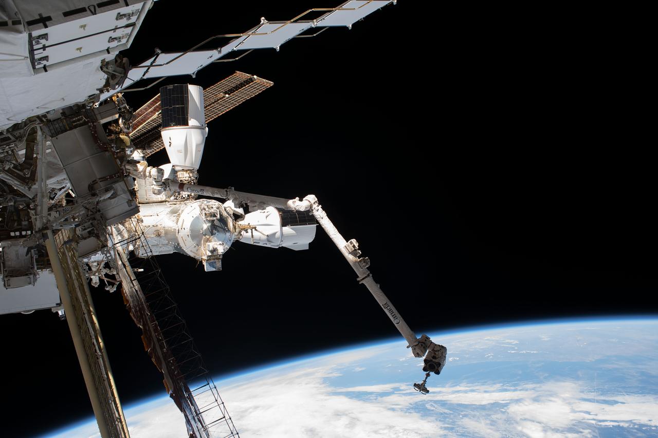 iss069e020758 (June 15, 2023) --- This photograph of the International Space Station was taken by NASA astronaut Woody Hoburg as he worked on the Starboard-6 truss structure during a spacewalk. The SpaceX Dragon cargo vehicle is pictured docked to the Harmony module's space-facing port and the SpaceX Dragon crew vehicle docked to Harmony's forward port. In the foreground, is the Canadarm2 robotic arm.