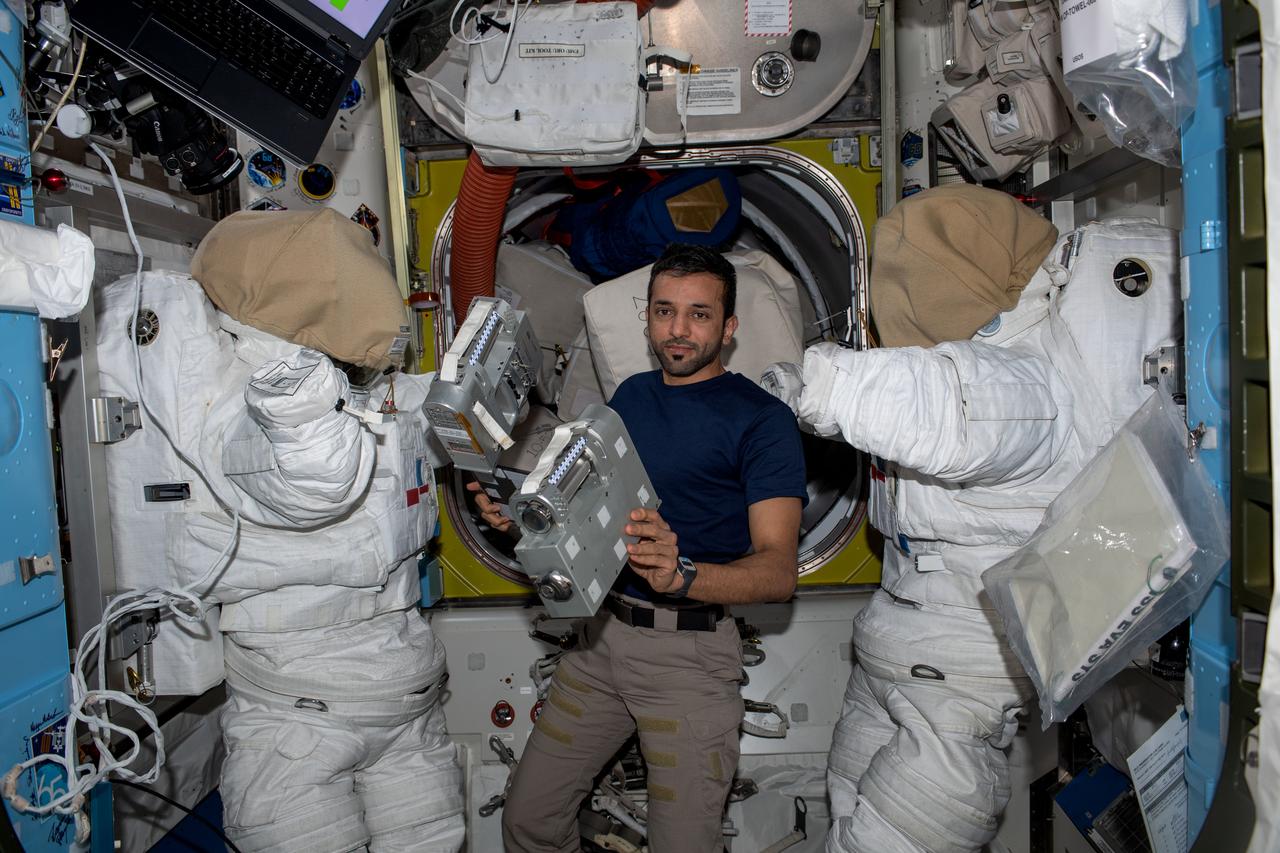 iss069e029779 (July 6, 2023) --- UAE (United Arab Emirates) astronaut and Expedition 69 Flight Engineer Sultan Alneyadi is pictured in between a pair of spacesuits while working on hardware maintenance inside the International Space Station's Quest airlock.