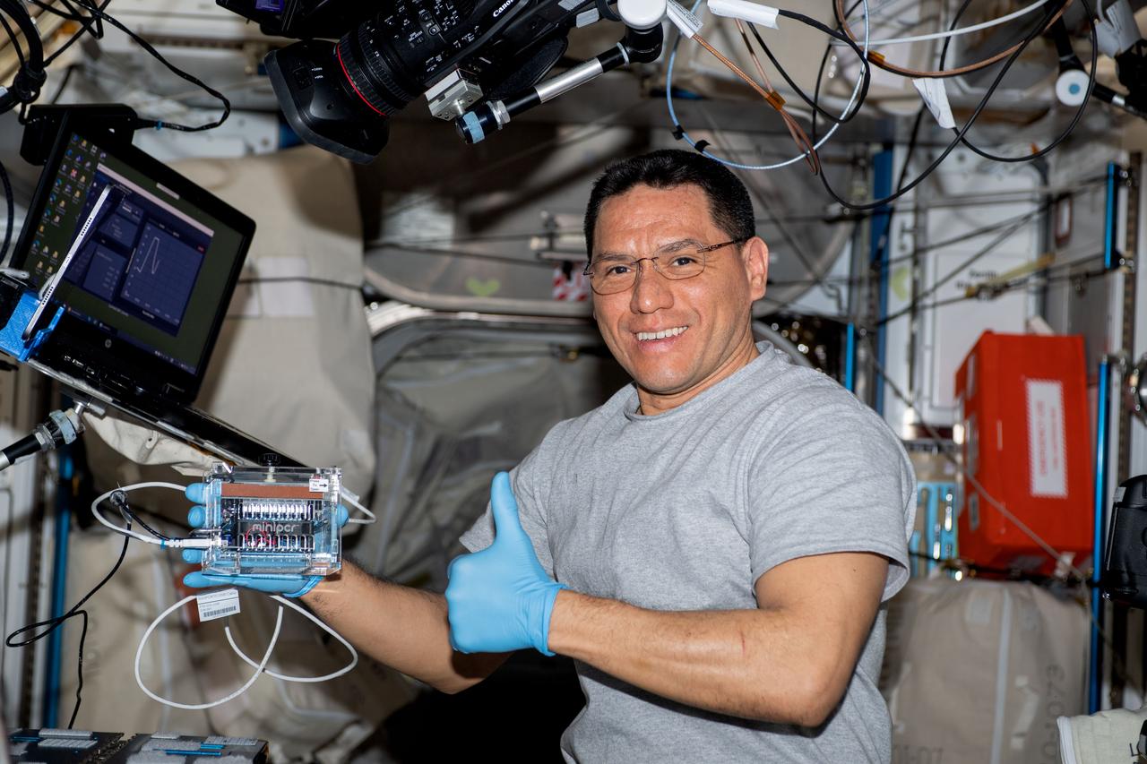 iss069e031305 (July 13, 2023) -- NASA astronaut and Expedition 69 Flight Engineer Frank Rubio holds the Mini Polymerase Chain Reaction (miniPCR) system, that promotes DNA research on Earth and in space, set up inside the Columbus laboratory module.