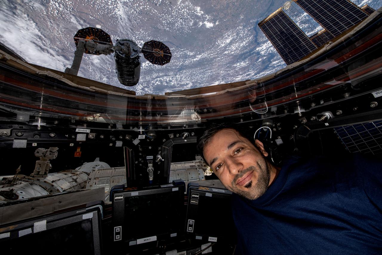 iss069e053771 (Aug. 4, 2023) --- UAE (United Arab Emirates) astronaut and Expedition 69 Flight Engineer Sultan Alneyadi is pictured in the International Space Station's cupola with Northrop Grumman's Cygnus cargo craft outside in the grips of the Canadarm2 robotic arm.