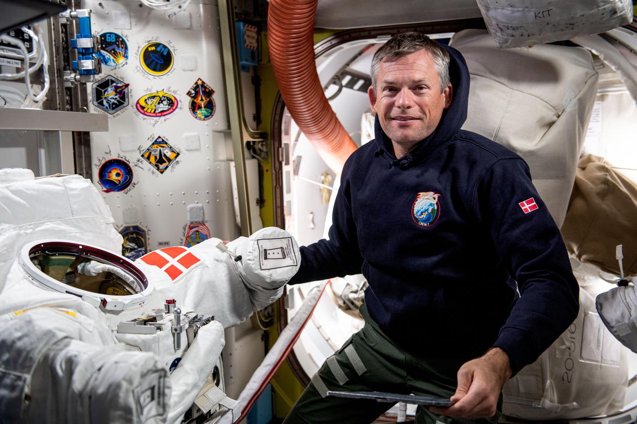 iss070e000500 (Sept. 29, 2023) --- ESA (European Space Agency) astronaut and Expedition 70 Commander Andreas Mogensen works on a spacesuit with his nation's flag patch (Mogensen is from Denmark) inside the Quest airlock aboard the International Space Station.