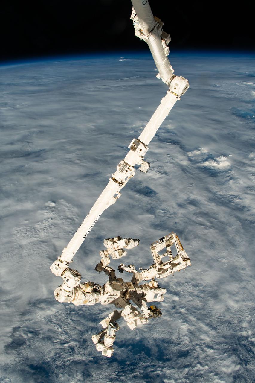 iss070e025899 (Nov. 15, 2023) --- The Canadarm2 robotic arm with its fine-tuned robotic hand, also known as Dextre, attached extends vertically down from the International Space Station as it orbited 261 miles above a cloudy Pacific Ocean north of Papua New Guinea.