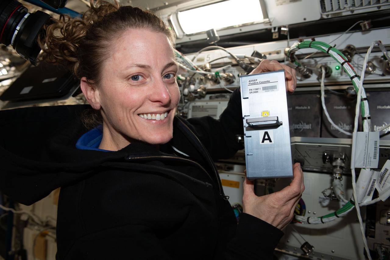 iss070e037585 (Dec. 11, 2023) --- NASA astronaut and Expedition 70 Flught Engineer Loral O'Hara shows off research hardware supporting the UMAMI, or Understanding of Microgravity on Animal-Microbe Interaction, space biology experiment. O'Hara is holdng the Avanced Space Experiment Processor (ADSEP) Fluid Processing Cassette (FPC) that supports the observation of the effects of spaceflight on the molecular and chemical interactions between beneficial microbes and their animal hosts.