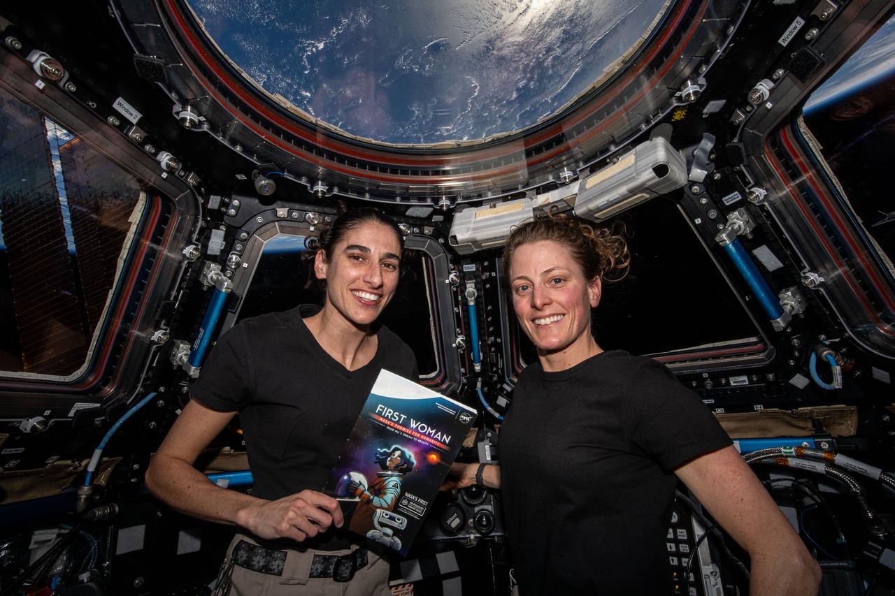 iss070e064628 (Jan. 12, 2024) --- Expeditin 70 Flight Engineers (from left) Jasmin Moghbeli and Loral O'Hara, both NASA astronauts, are pictured inside the International Space Station's cupola holding NASA's first graphic novel, "The First Woman."