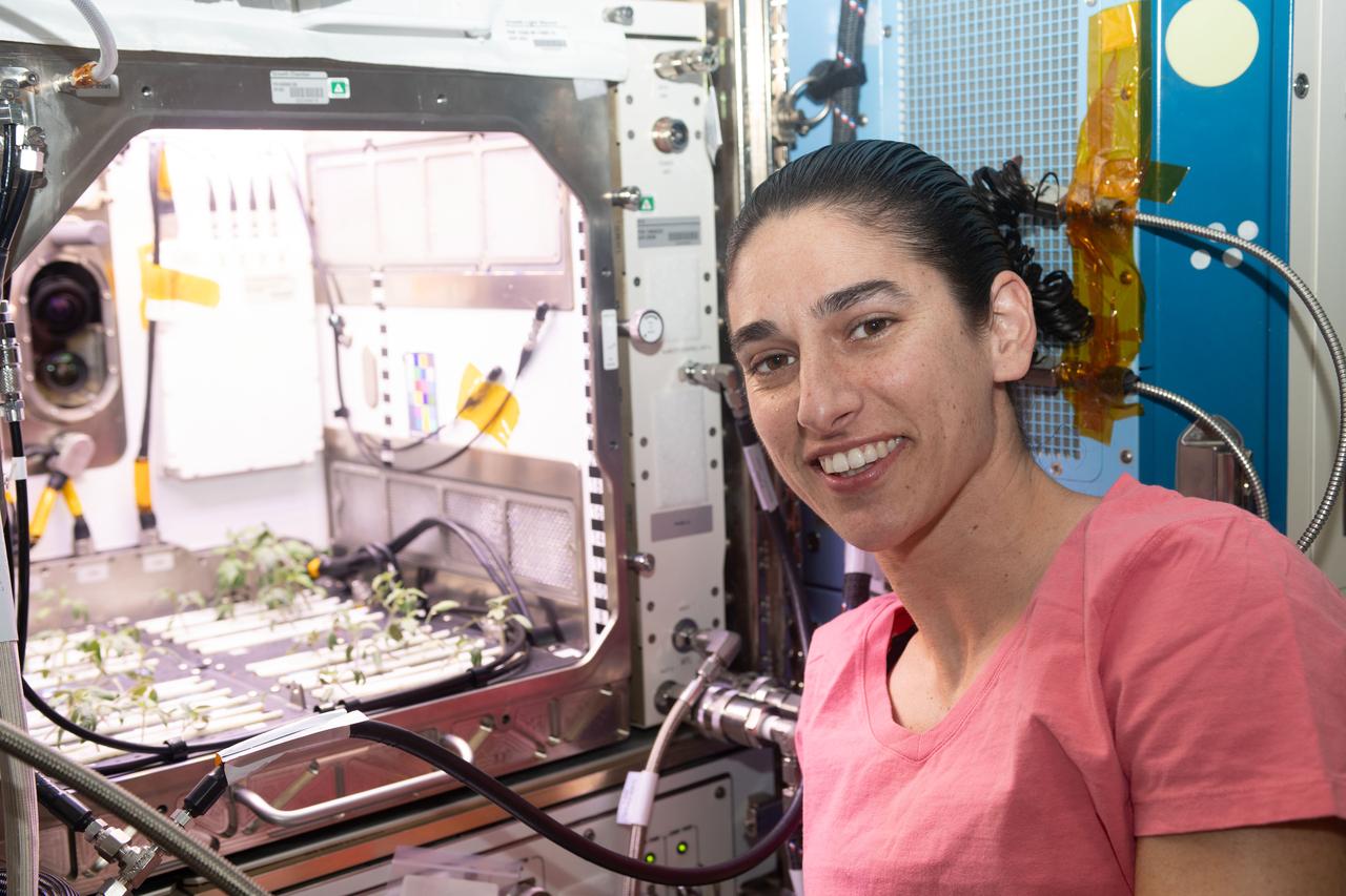 iss070e068950 (Jan. 18, 2024) --- NASA astronaut and Expedition 70 Flight Engineer Jasmin Moghbeli poses in front of the Kibo laboratory module's Advanced Plant Habitat housing tomato plants for an experiment investigating how the plant immune system adapts to spaceflight and how spaceflight affects plant production.