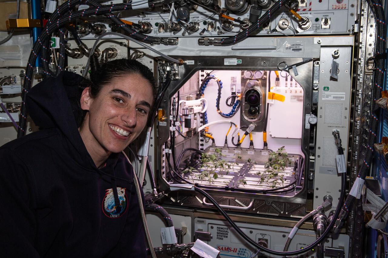 iss070e073612 (Jan. 18, 2024) --- NASA astronaut and Expedition 70 Flight Engineer Jasmin Moghbeli poses in front of the Kibo laboratory module's Advanced Plant Habitat housing tomato plants for an experiment investigating how the plant immune system adapts to spaceflight and how spaceflight affects plant production.