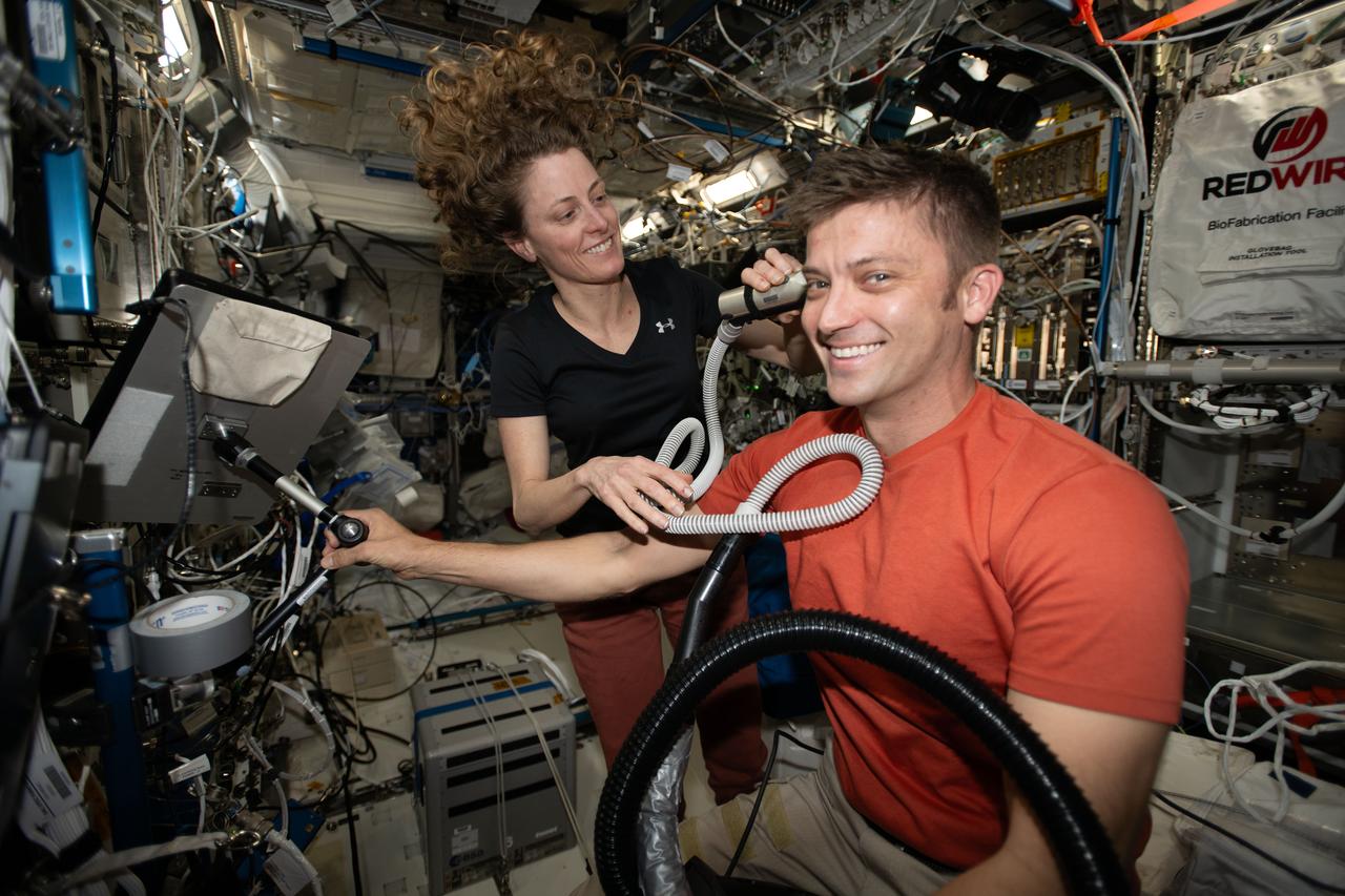 iss070e118934 (March 17, 2024) --- Expedition 70 Flight Engineers Loral O'Hara and Matthew Dominick, both NASA astronauts, are pictured as Dominick receives a haircut from O'Hara who is using an electric razor with a vacuum attached that collects the loose hair.