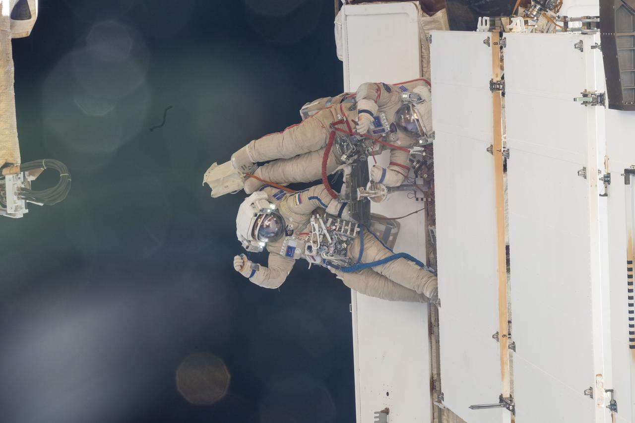 iss071e045508 (April 25, 2024) --- Cosmonauts Nikolai Chub (waving) and Oleg Kononenko are pictured outside of the International Space Station wearing their Orlan spacesuits during a four-hour and 36-minute spacewalk. During their excursion they worked on the Russian segment of the complex completing the deployment of one panel on a synthetic radar communications system. The duo also installed equipment and experiments to analyze the level of corrosion on station surfaces and modules.