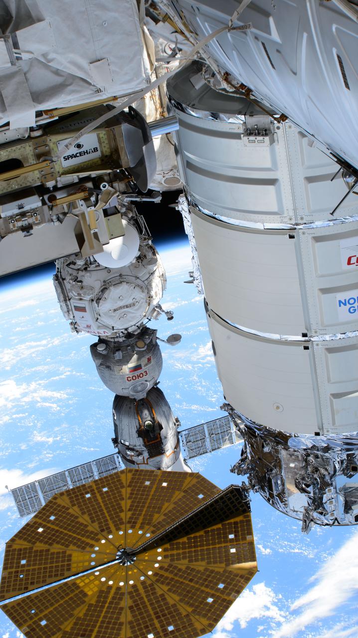 iss071e243431 (June 28, 2024) --- Pictured in the foreground, is Northrop Grumman's Cygnus space freighter, berthed to the International Space Station's Unity module, and one of two of its cymbal-shaped UltraFlex solar arrays. In the rear, is the Soyuz MS-25 crew ship docked to the Prichal docking module. The orbital outpost was soaring 263 miles above the Pacific Ocean south of Midway Atoll.