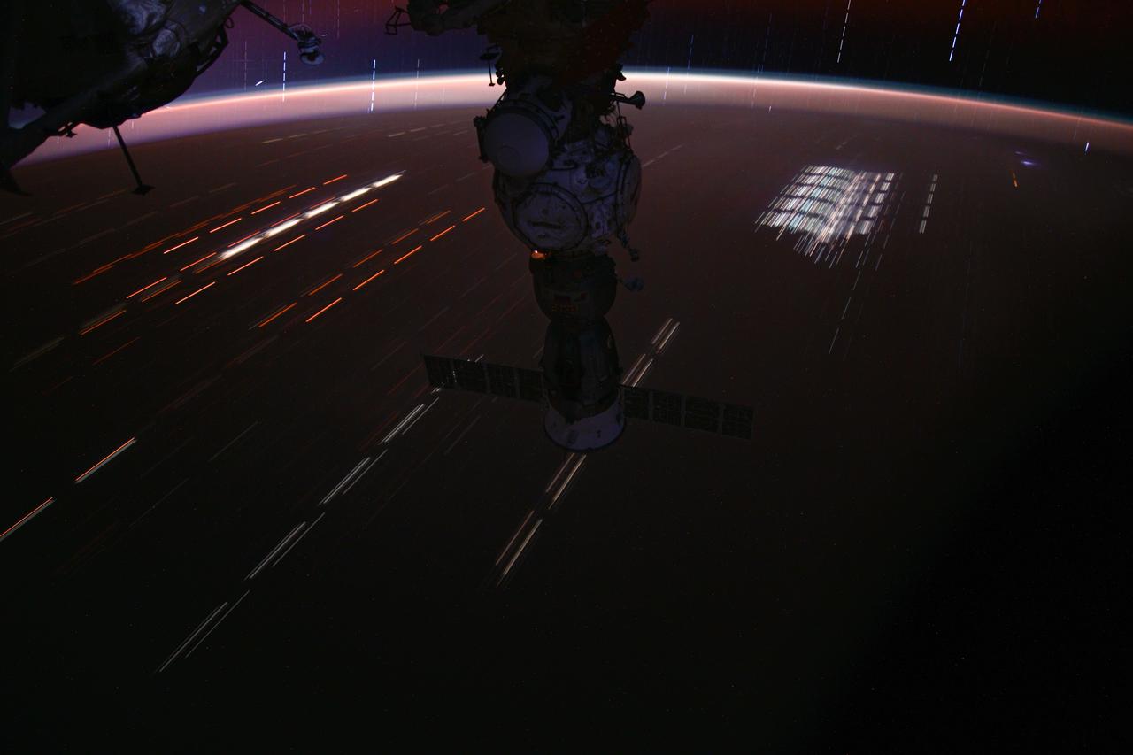 iss071e414590_stk (Aug. 3, 2024) --- This long-duration photograph of the Soyuz MS-25 spacecraft with light trails on Earth below and stars trails above the horizon was taken by NASA astronaut Matthew Dominick as the International Space Station soared 262 miles above a sparsely populated region of Queensland, Australia.