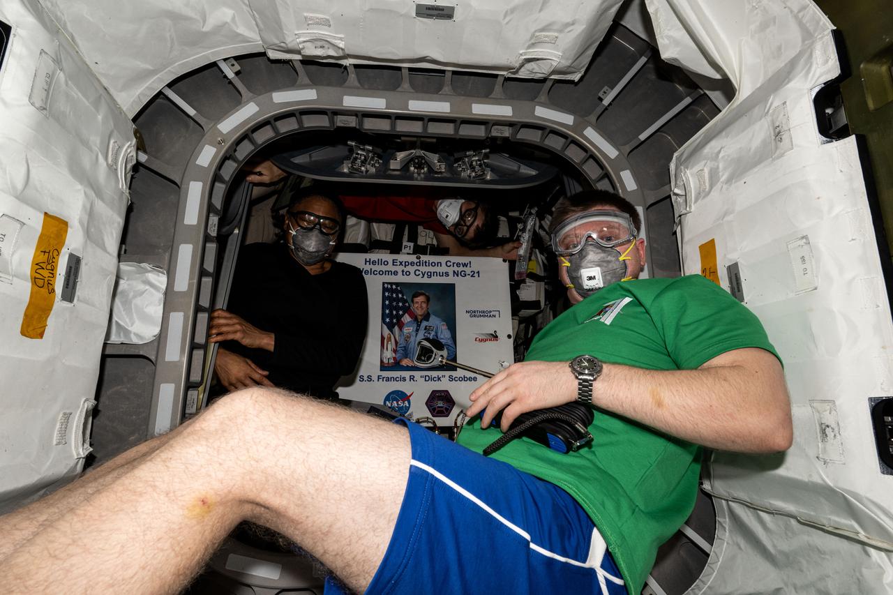 iss071e462164 (Aug. 6, 2024) --- NASA astronauts (from left) Jeanette Epps and Matthew Dominick, both Expedition 71 Flight Engineers, are pictured wearing personal protective equipment (PPE) shortly after entering the Northrop Grumman Cygnus space freighter. Inside Cygnus is a poster of former NASA astronaut Francis R. "Dick" Scobee for whom the spacecraft is named after. The duo was wearing PPE after opening the hatch and entering the vehicle to protect against potential dust or debris that may have dislodged during Cygnus' launch and ascent to space.