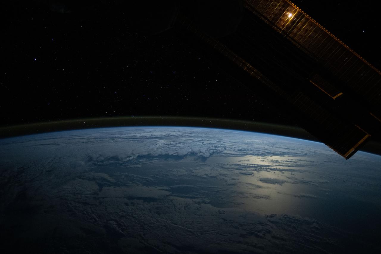 iss071e456772 (July 18, 2024) --- The Moon's glint beams off the Pacific Ocean as stars glitter in the background above the Earth's airglow. The Moon is obscured behind a solar array in this photograph from the International Space Station as it orbited 264 miles above.