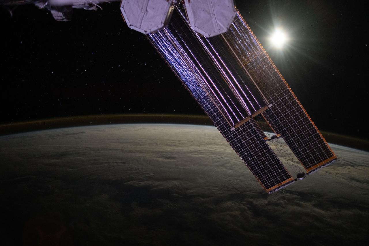 iss071e457356 (July 18, 2024) --- The Moon illuminates a cloud-covered Pacific Ocean as stars glitter in the background above the Earth's airglow. The International Space Station's solar arrays dominate the foreground as the orbital outpost soared 268 miles above.