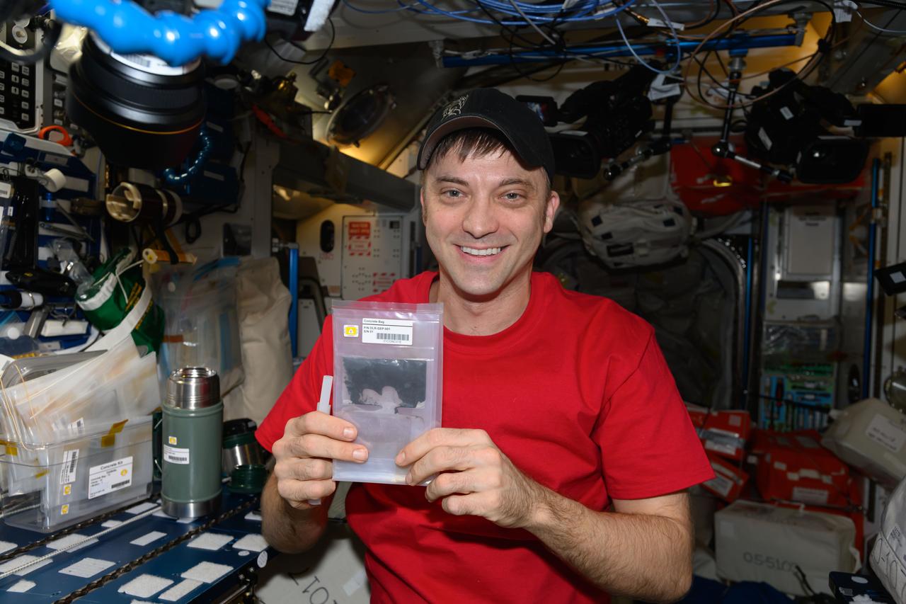 iss071e462520 (Aug. 12, 2024) --- NASA astronaut and Expedition 71 Flight Engineer Matthew Dominick displays a bag containing simulated lunar soil and other materials mixed with a liquid solution. He was exploring how microgravity affects the production of cement materials that could be used to build infrastructure on the lunar surface.