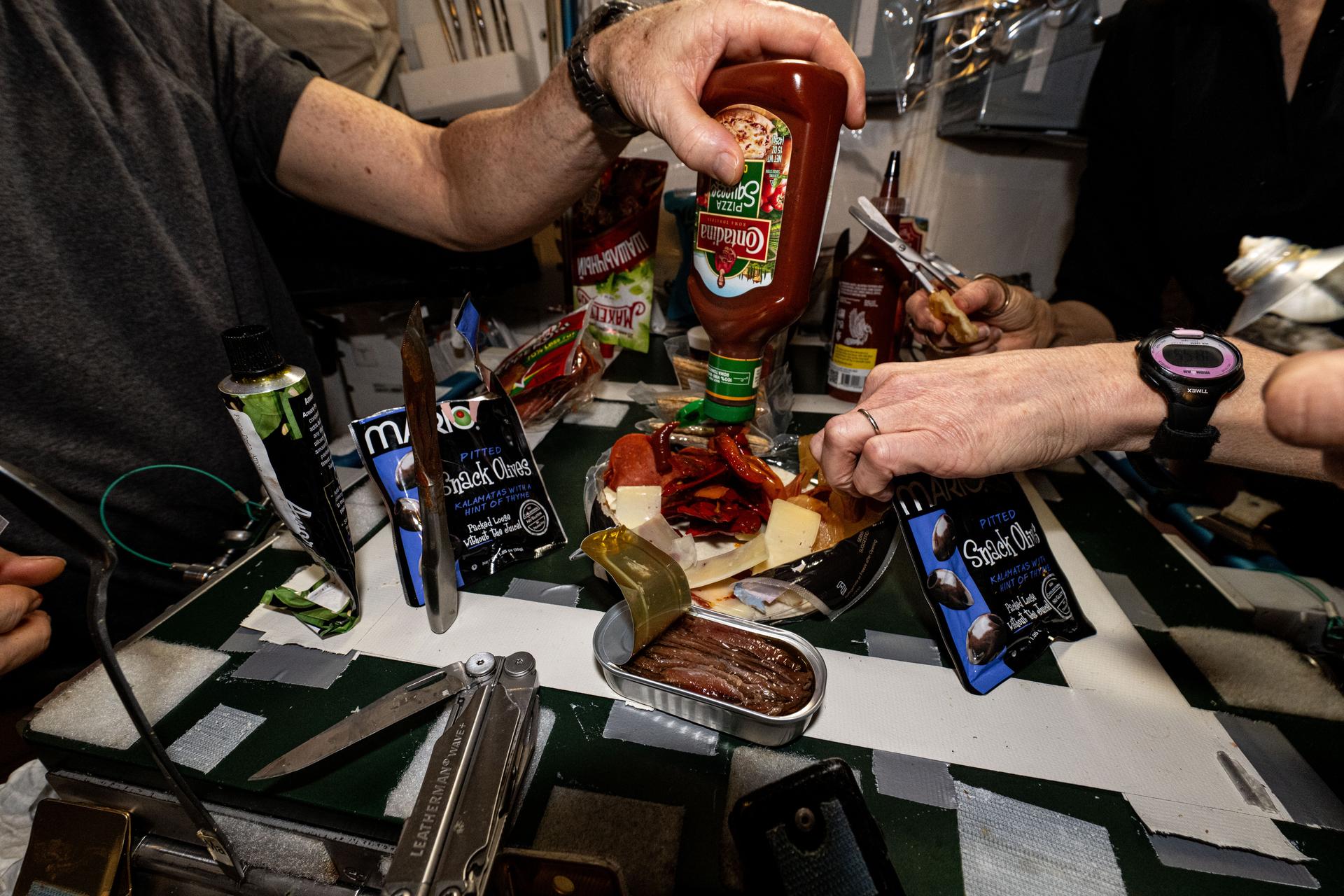 Astronauts show off ingredients while making pizza aboard the International Space Station's galley located inside the Unity module. Items are attached to the galley using tape and velcro to keep them from flying away in the microgravity environment.