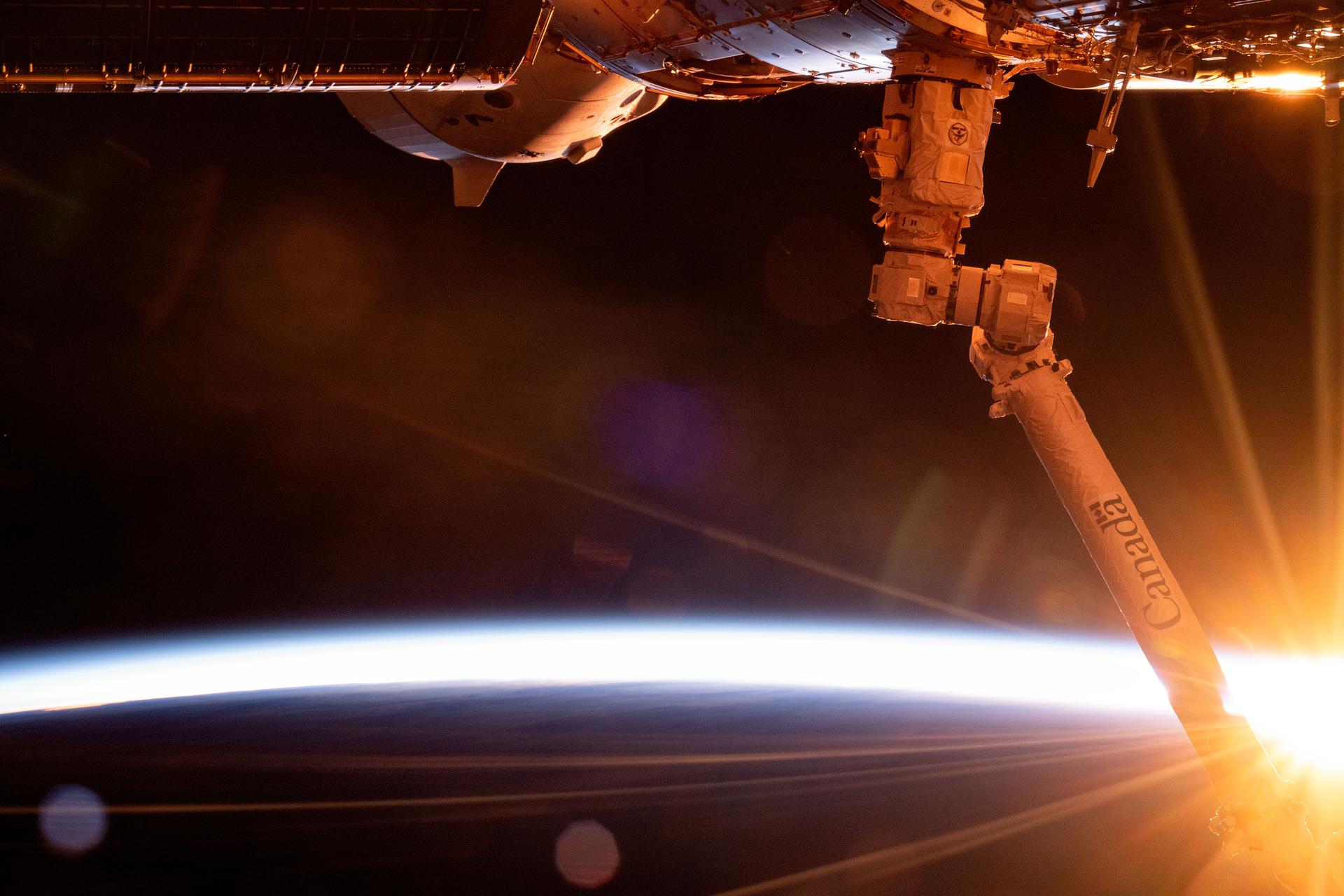 The first rays of an orbital sunrise breakthrough illuminating Earth's atmosphere in this photograph from the International Space Station as it orbited 272 miles above the South Pacifc Ocean off the southern coast of New Zealand. In the foreground, at right, is the Canadarm2 robotic arm and partially obscured at top, is the SpaceX Dragon Freedom spacecract docked to the Harmony module's forward port.