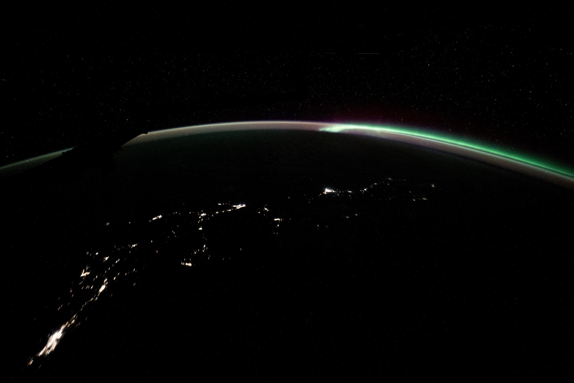 The aurora australis blends with Earth's atmospheric glow blanketing the nighttime horizon with New Zealand's city lights below in this photograph from the International Space Station as it orbited 270 miles above the Tasman Sea.