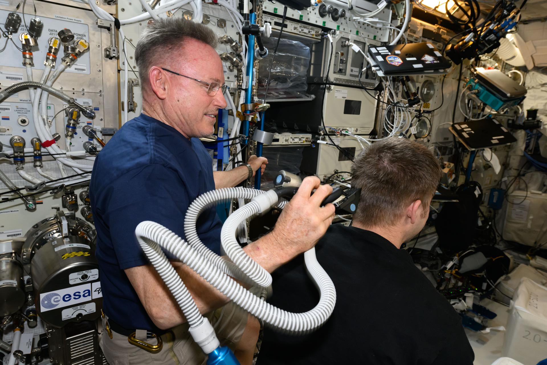 It's haircut day on the International Space Station. Expedition 72 Flight Engineer Butch Wilmore trims Expedition 72 Flight Engineer Matthew Dominck's hair using an electric razor with a vacuum attached that collects the loose hair.
