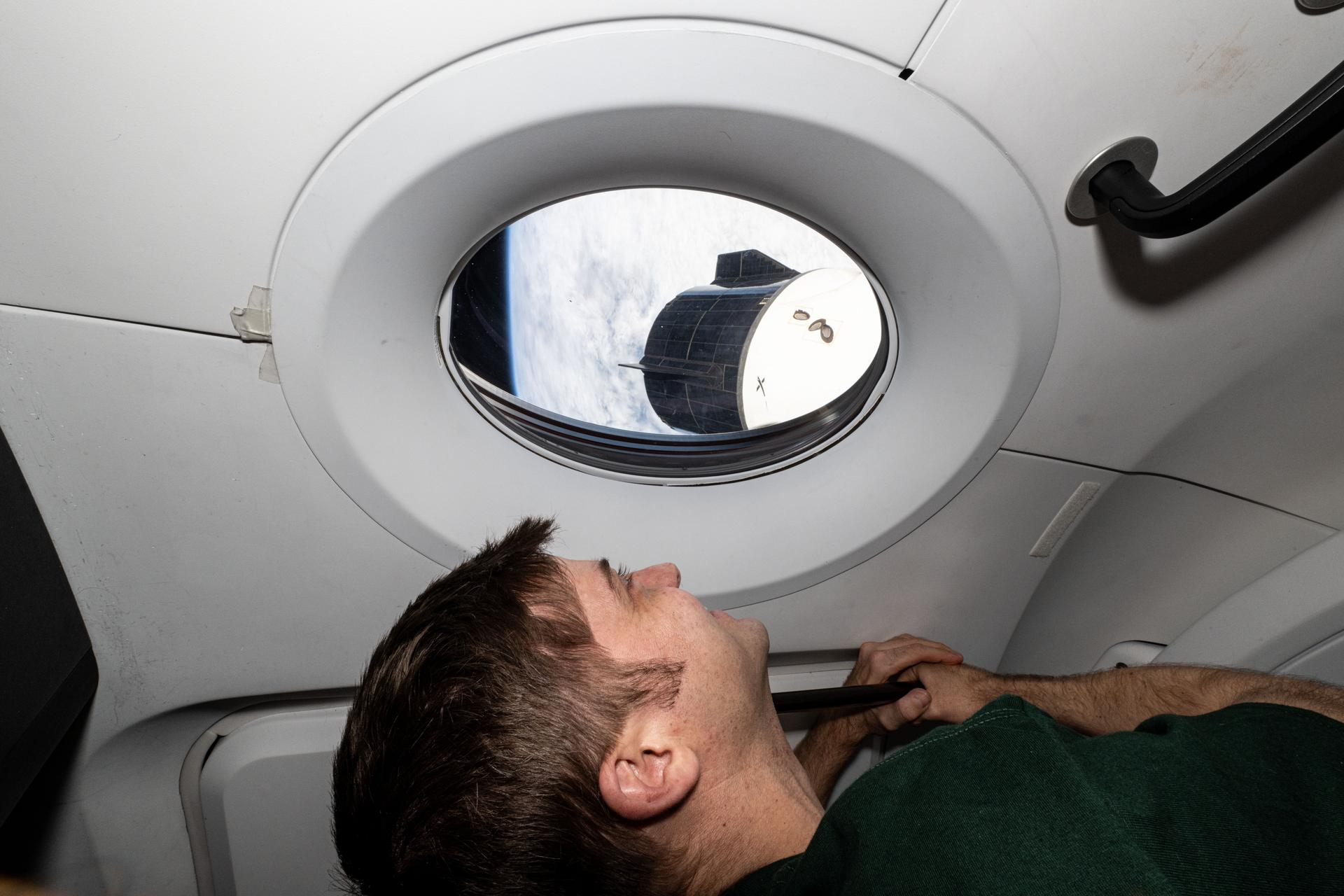 NASA astronaut and Expedition 72 Flight Engineer Matthew Dominick looks out a window on the SpaceX Dragon Endeavour spacecraft as the International Space Station orbited 267 miles above the Pacific Ocean of the coast of Chile. Just outside Endeavour's window is the Dragon Freedom spacecraft.