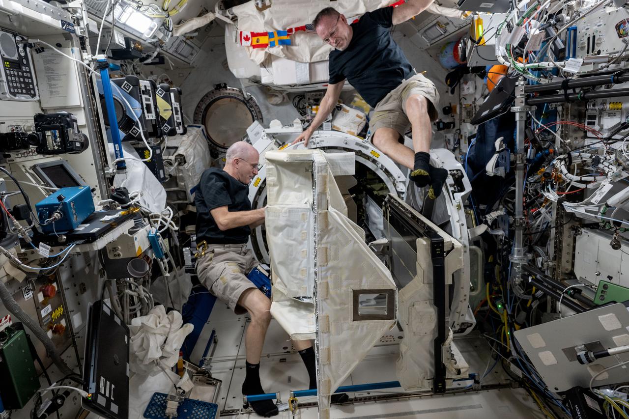 iss072e143154 (Oct. 30, 2024) --- Expedition 72 Flight Engineers (from left) Don Pettit and Butch Wilmore, both NASA astronauts, remove a small satellite deployer from inside the Kibo laboratory module's airlock that had earlier deployed several CubeSats into Earth orbit for a series of technology studies.