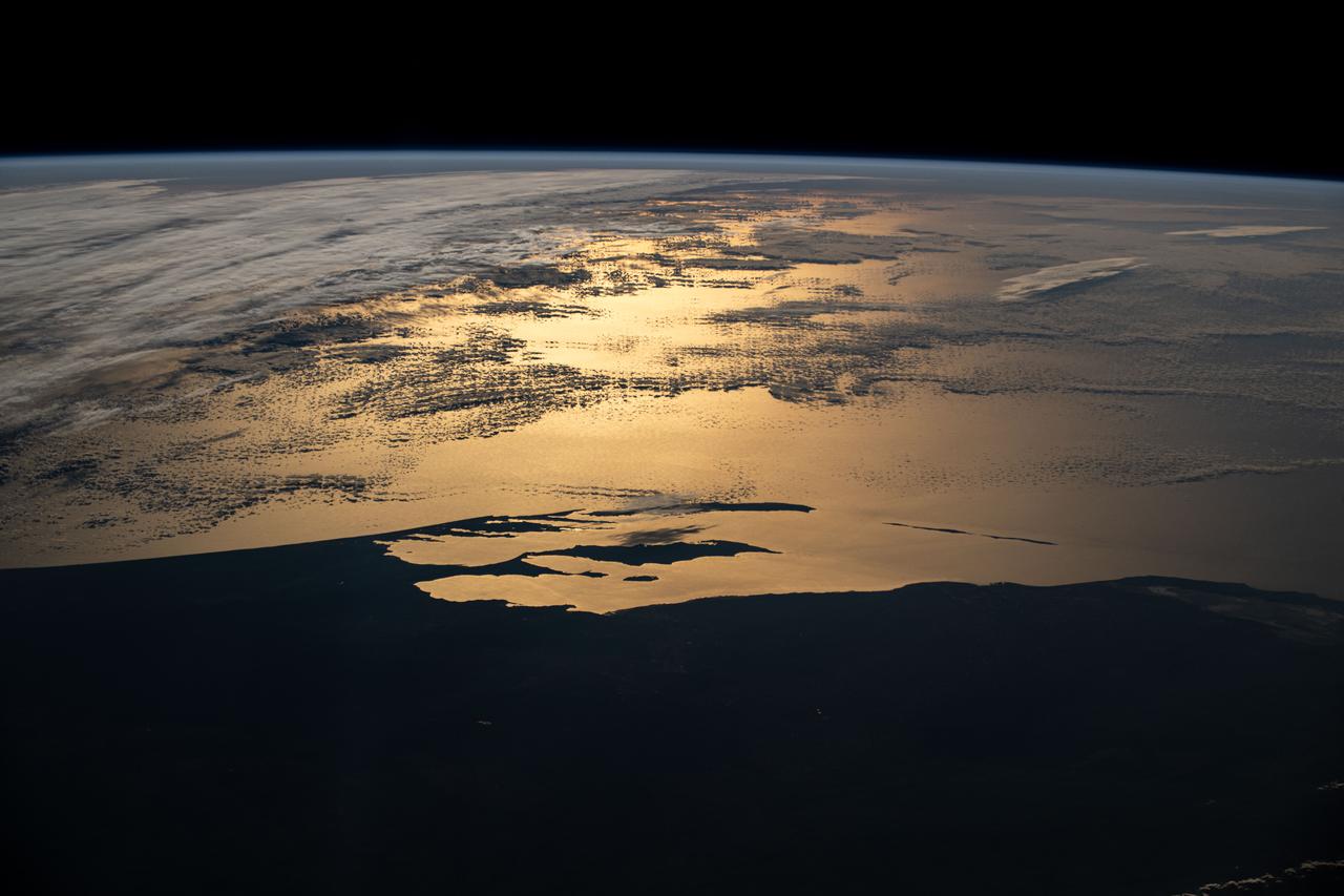 iss072e145182 (Nov. 5, 2024) --- Western Australia's silhouetted coastline contrasts with the sun's golden-hued glint beaming off a partly cloudy Indian Ocean in this photograph from the International Space Station as it orbited 265 miles above the island continent during an orbital sunset.