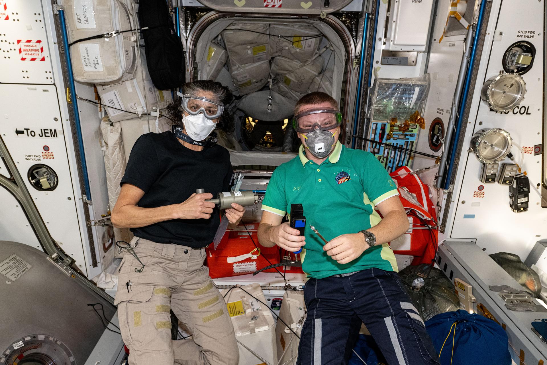 Expedition 72 Commander Suni Williams (left) from NASA and Flight Engineer Aleksandr Gorbunov from Roscosmos wear personal protective equipment shortly after the hatches opened to the newly arrived SpaceX Dragon cargo spacecraft. Crew members wear facemasks and eye shields when entering a cargo craft for the first time to shield against potential dust or debris that may have dislodged during the spacecraft's ascent to orbit. Dragon had automatically docked to the International Space Station's forward port on the Harmony module just over two hours before this photograph was taken.