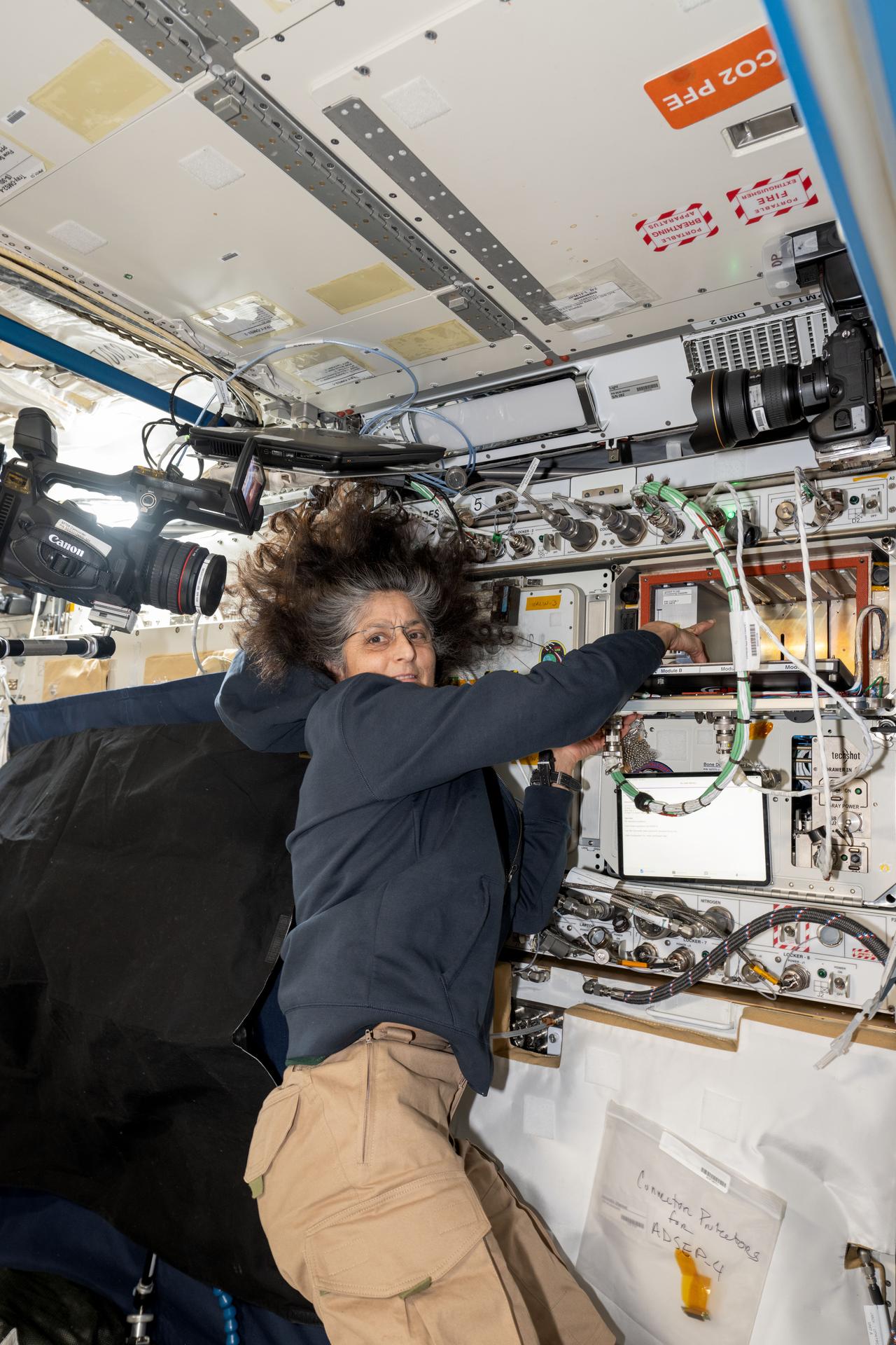 NASA astronaut and Expedition 72 Commander Suni Williams points to the Advanced Space Experiment Processor-4 (ADSEP-4), a sample processor that can perform research operations on the SpaceX Dragon cargo spacecraft, the Northrop Grumman Cygnus cargo spacecraft, and the International Space Station.