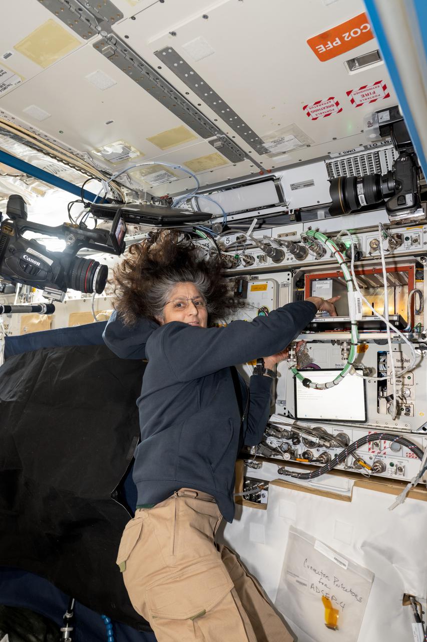 iss072e146339 (Nov. 7, 2024) --- NASA astronaut and Expedition 72 Commander Suni Williams points to the Advanced Space Experiment Processor-4 (ADSEP-4), a sample processor that can perform research operations on the SpaceX Dragon cargo spacecraft, the Northrop Grumman Cygnus cargo spacecraft, and the International Space Station.