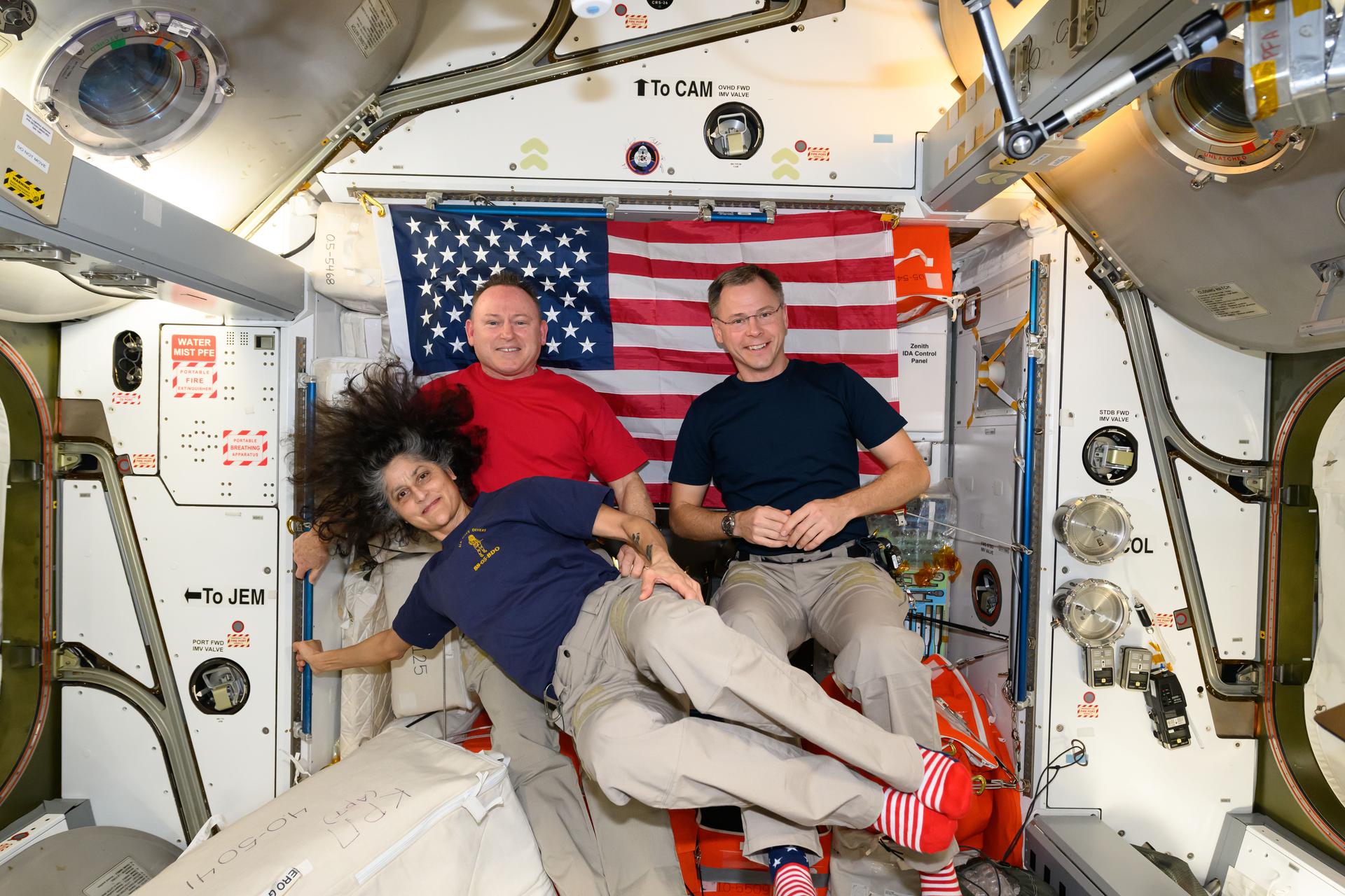 Expedition 72 Commander Suni Williams and Flight Engineers Butch Wilmore and Nick Hague, all three NASA astronauts, pose for a portrait together with the U.S. flag behind them aboard the International Space Station's Harmony module. The trio was honoring veteran members of the U.S. Armed Forces during Veteran's Day. Williams is a retired U.S. Navy captain, Wilmore is a U.S. Navy test pilot, and Hague is U.S. Space Force colonel.