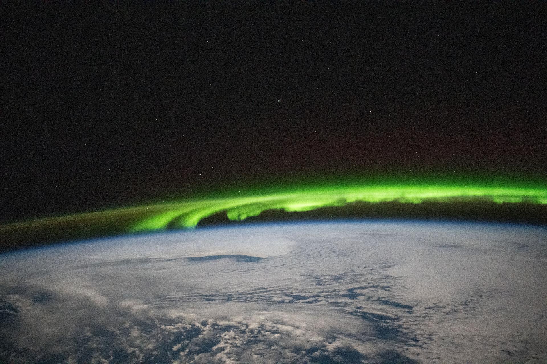 A bright green aurora borealis streams above Earth's surface as the International Space Station orbited 269 miles above a cloudy North Pacific Ocean south of Alaska's Aleutian Islands.