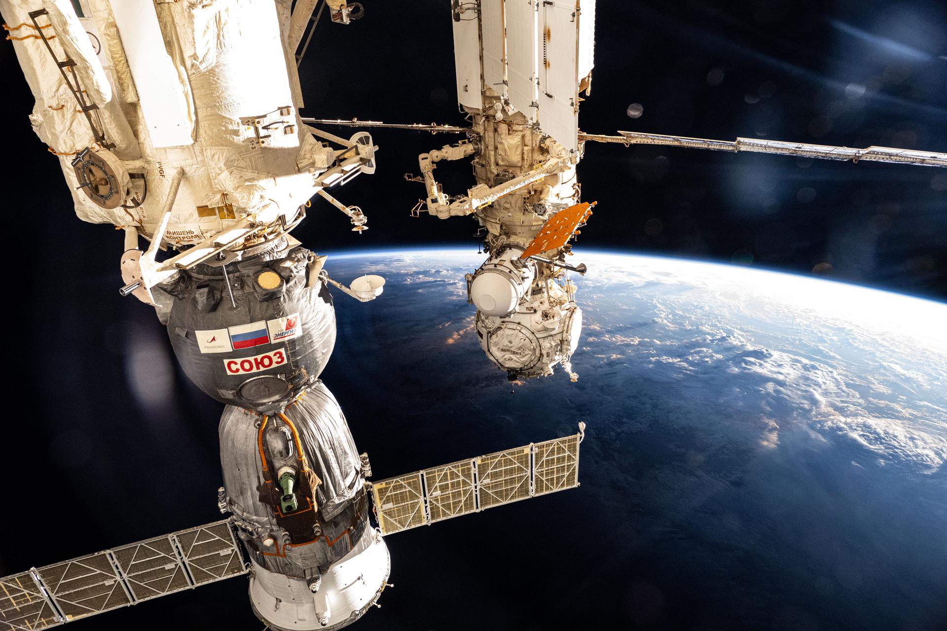 The International Space Station soars into an orbital sunset 259 miles above a cloudy Pacific Ocean northwest of the Hawaiian island chain. At left, the Soyuz MS-26 crew ship is pictured docked to the Rassvet module. At center, the Prichal docking module and the European robotic arm are pictured attached to the Nauka science module.