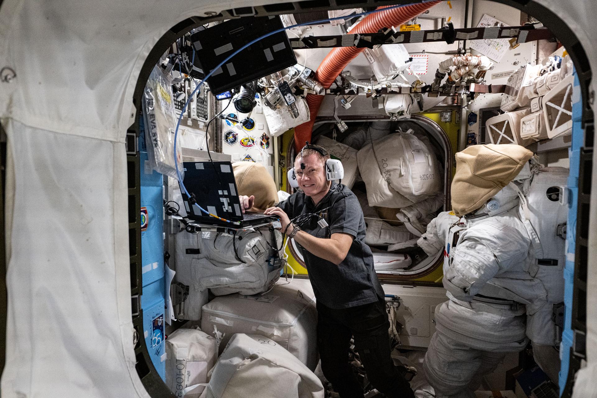 Roscosmos cosmonaut and Expedition 72 Flight Engineer Aleksandr Gorbunov wears headphones and conducts a hearing test in the quiet environment of the International Space Station's Quest airlock where spacesuits are stowed and spacewalks are staged.