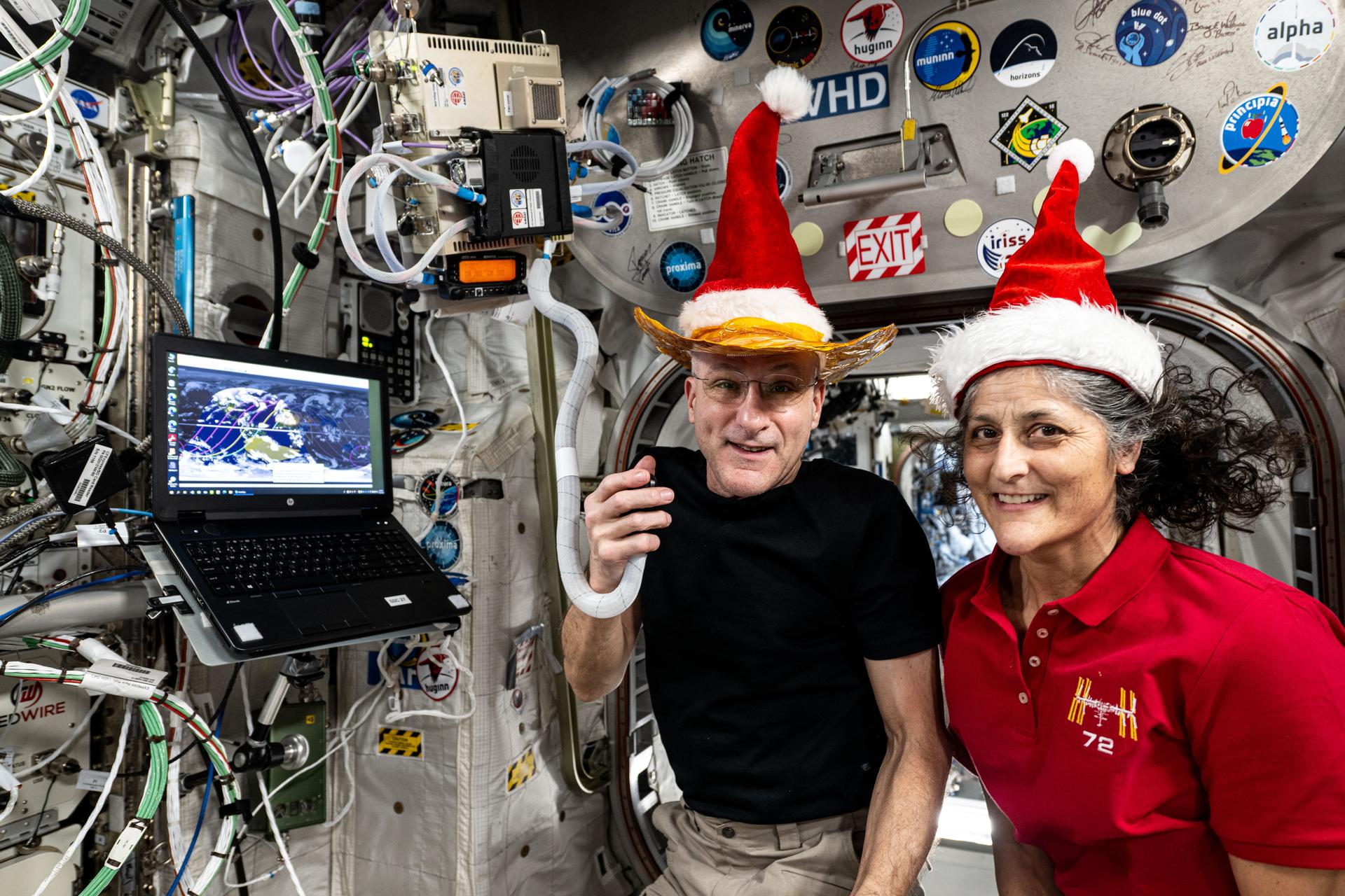 NASA astronauts Don Pettit and Suni Williams, Expedition 72 flight engineer and commander respectively, pose for a fun holiday season portrait while speaking on a ham radio inside the International Space Station's Columbus laboratory module.