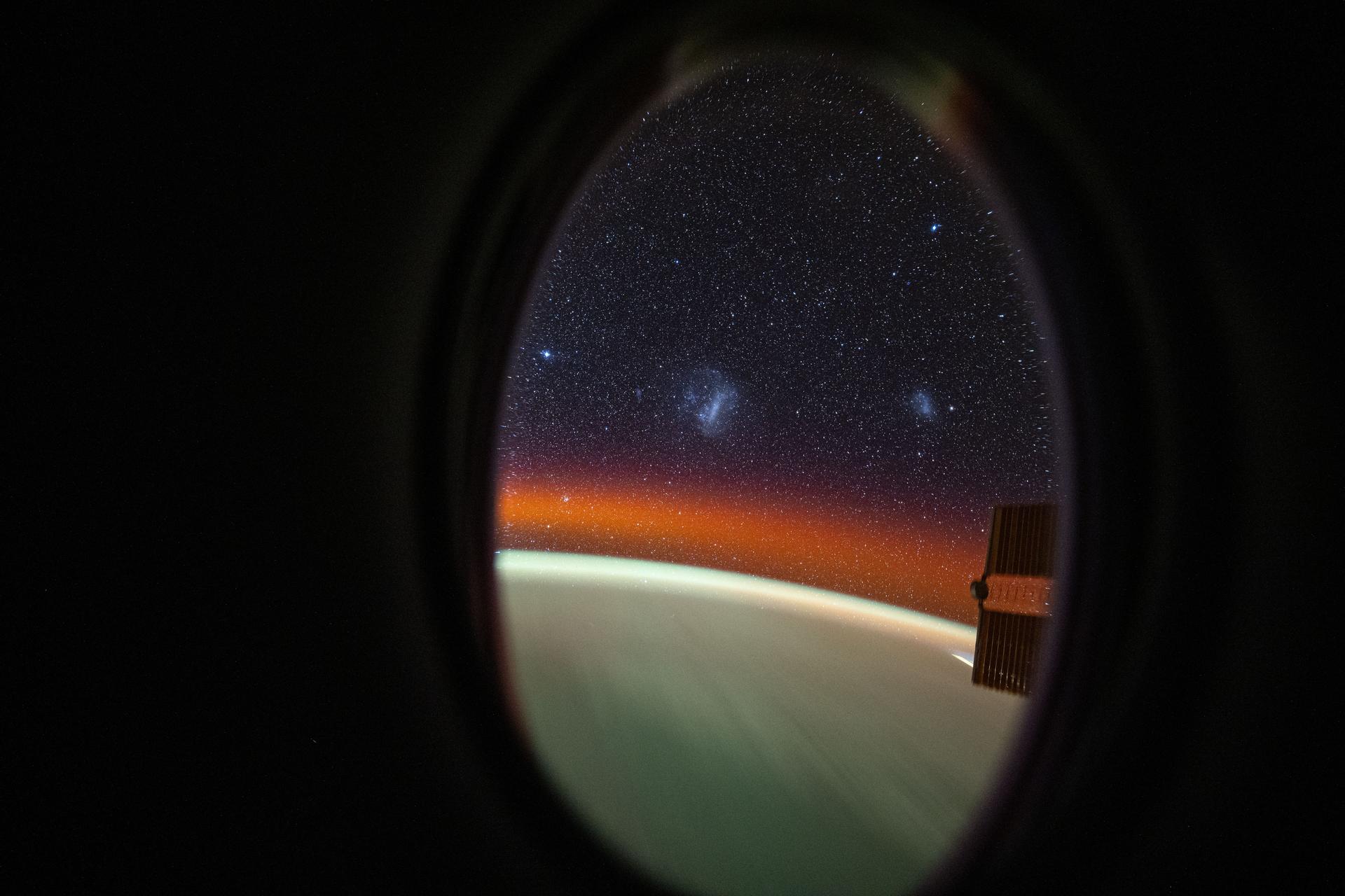 This long-duration photograph looks out a window on the SpaceX Dragon crew spacecraft to the Large and Small Magellanic Clouds, two irregular dwarf galaxies, as the International Space Station orbited 260 miles above the Pacific Ocean off the coast of Mexico.