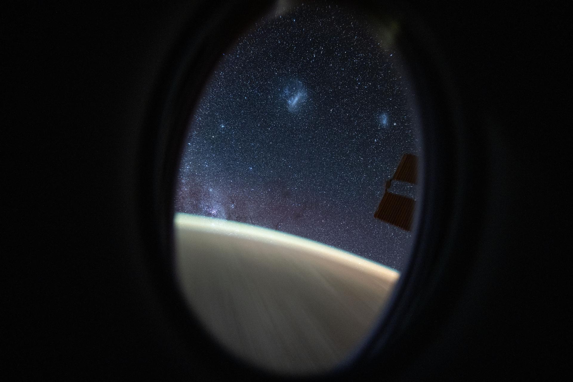 This long-duration photograph looks out a window on the SpaceX Dragon crew spacecraft to the Large and Small Magellanic Clouds, two irregular dwarf galaxies, as the International Space Station orbited 260 miles above the Pacific Ocean northeast of Australia.