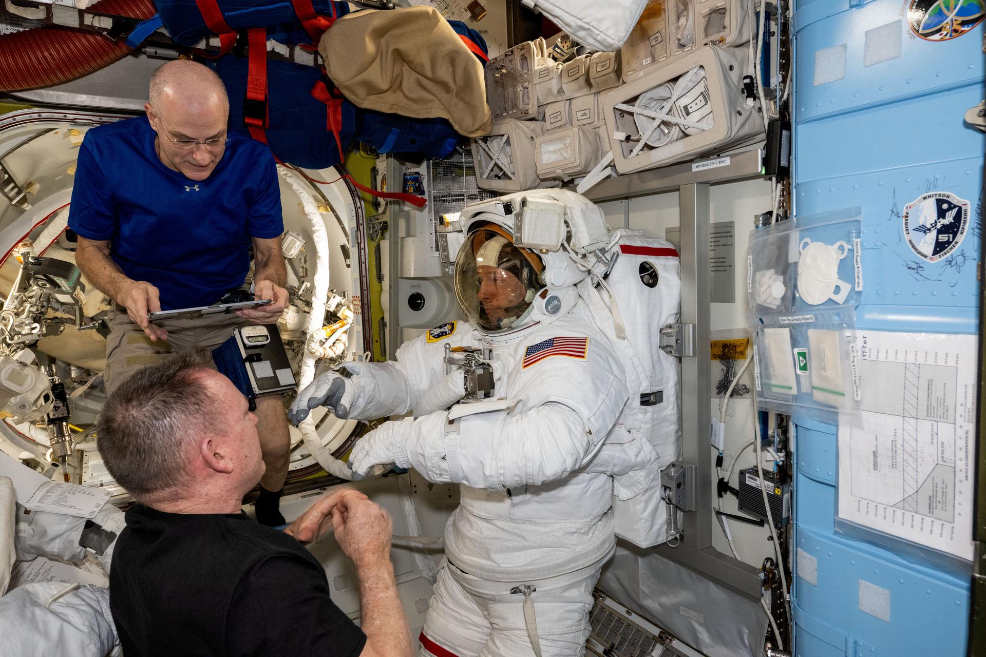 NASA astronauts Don Pettit (top) and Butch Wilmore (bottom) assist NASA astronaut Nick Hague (center) as he tries on and evaluates his spacesuit in a pressurized configuration aboard the International Space Station's Quest airlock.