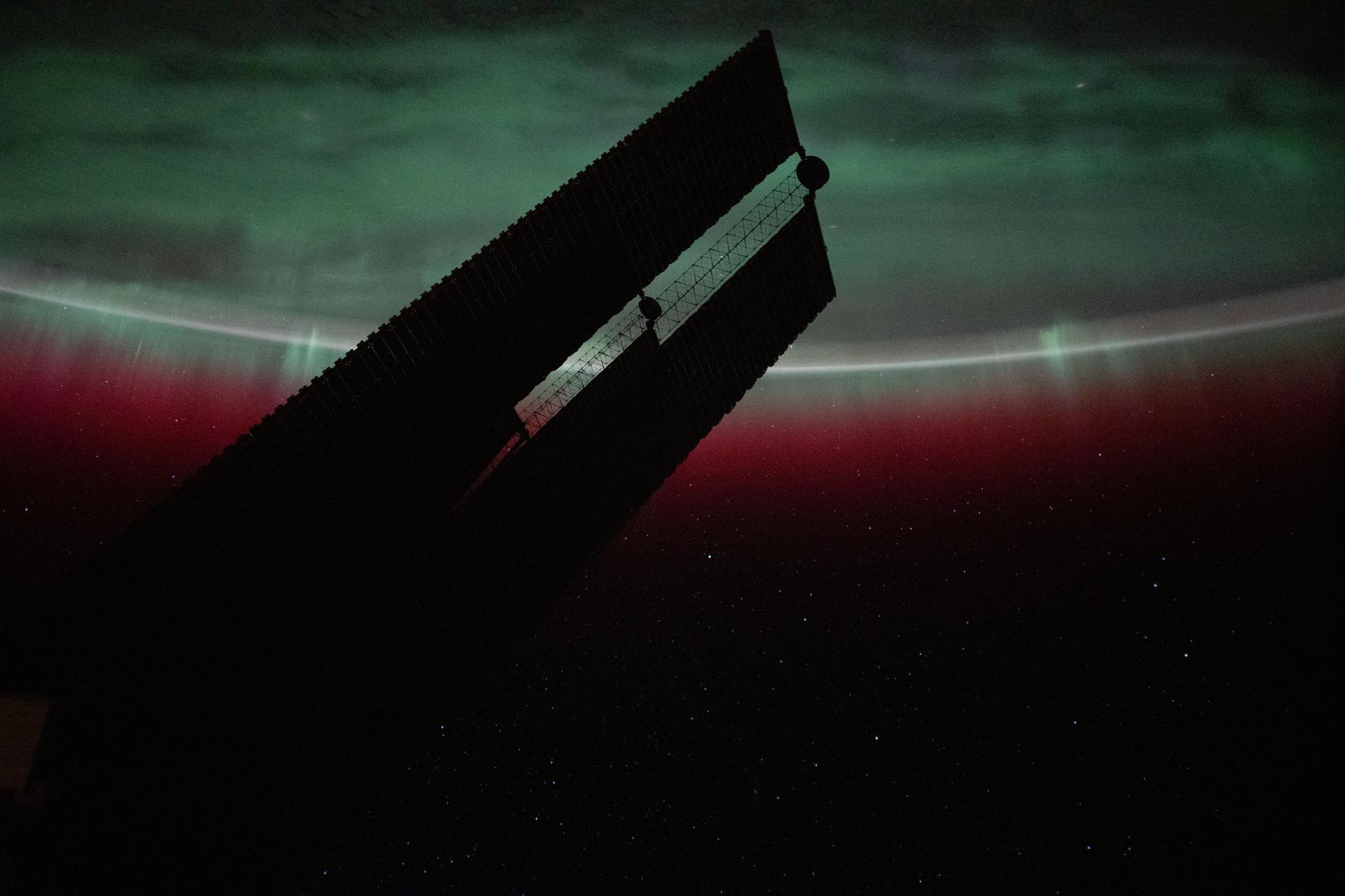 One of the International Space Station's main solar arrays is silhouetted against the backdrop of a green and red aurora borealis blanketing Quebec, Canada, as the orbital outpost soared 261 miles above.
