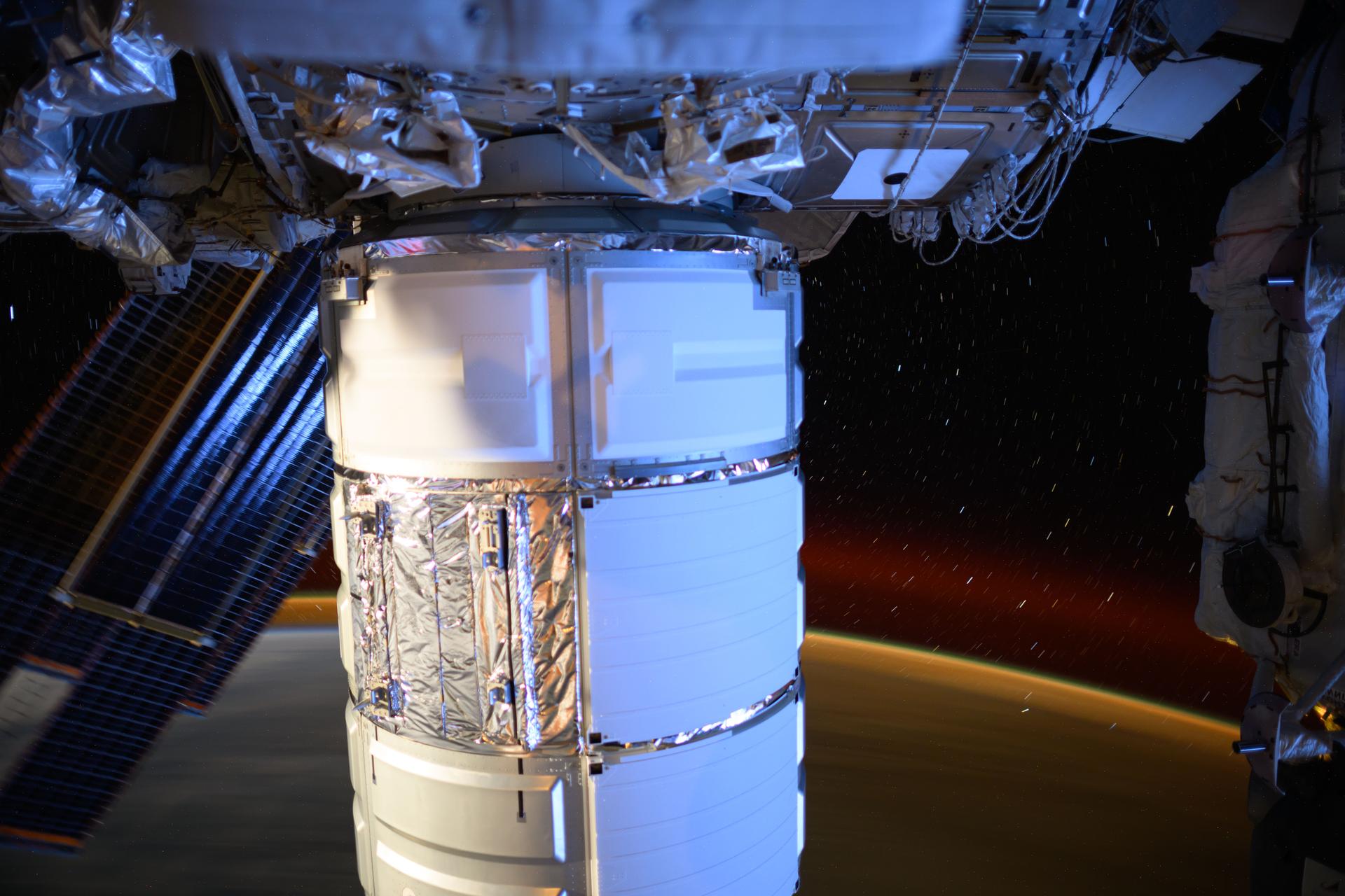 Northrop Grumman's Cygnus space freighter is pictured berthed to the International Space Station's Earth-facing port on the Unity module. This long-duration photograph also highlights Earth's atmospheric glow and star trails as the orbital outpost soared 262 miles above the North Atlantic Ocean.