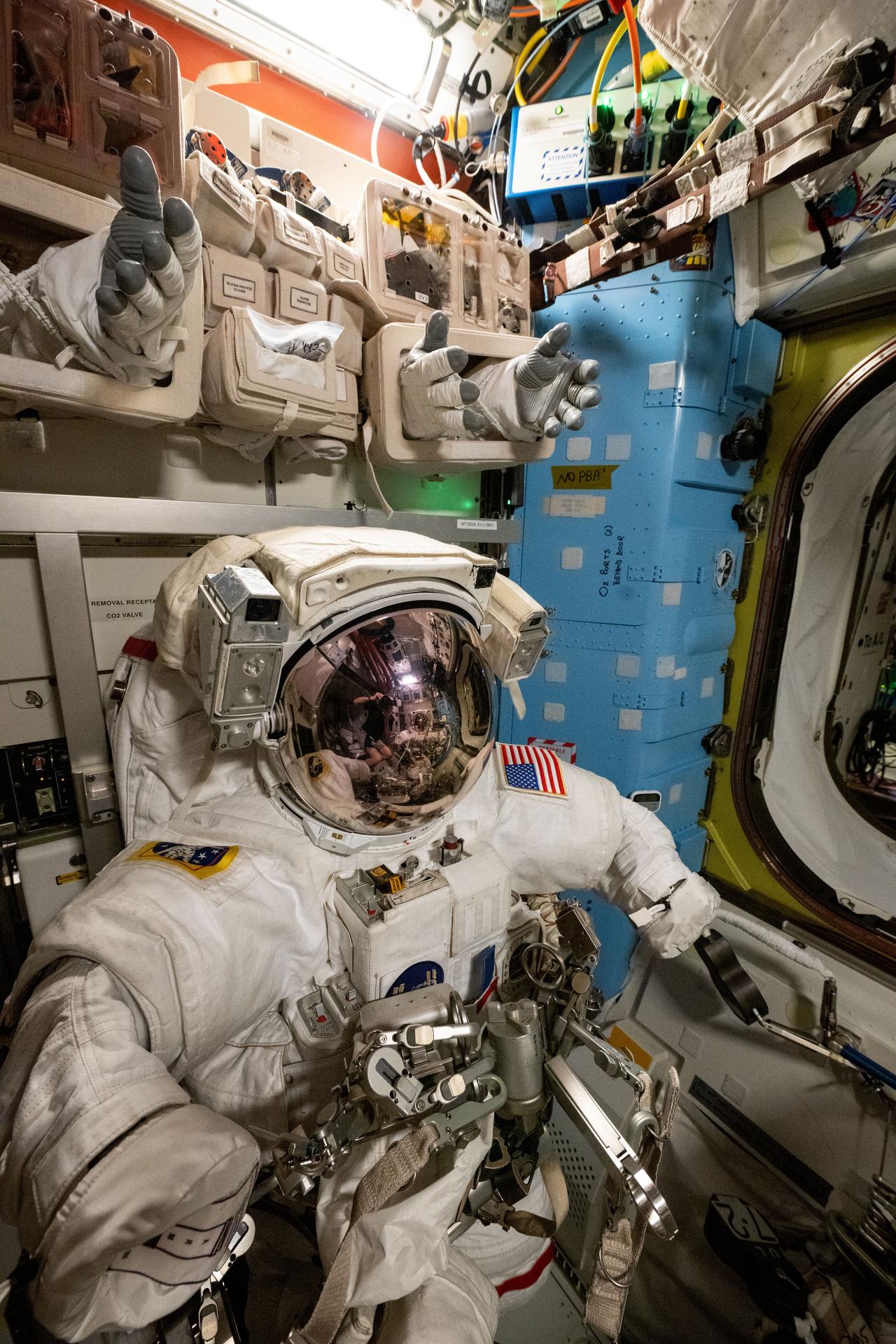 A spacesuit is pictured staged inside the International Space Station's Quest airlock ahead of a spacewalk planned for NASA astronauts Suni Williams and Butch Wilmore. The two spacewalkers are scheduled to exit the Quest airlock on Jan. 30 to remove a radio frequency group antenna assembly and search for microbes outside the orbital outpost. At top, spacesuit gloves are stowed above the spacesuits for easy access when astronauts are preparing to begin a spacewalk.