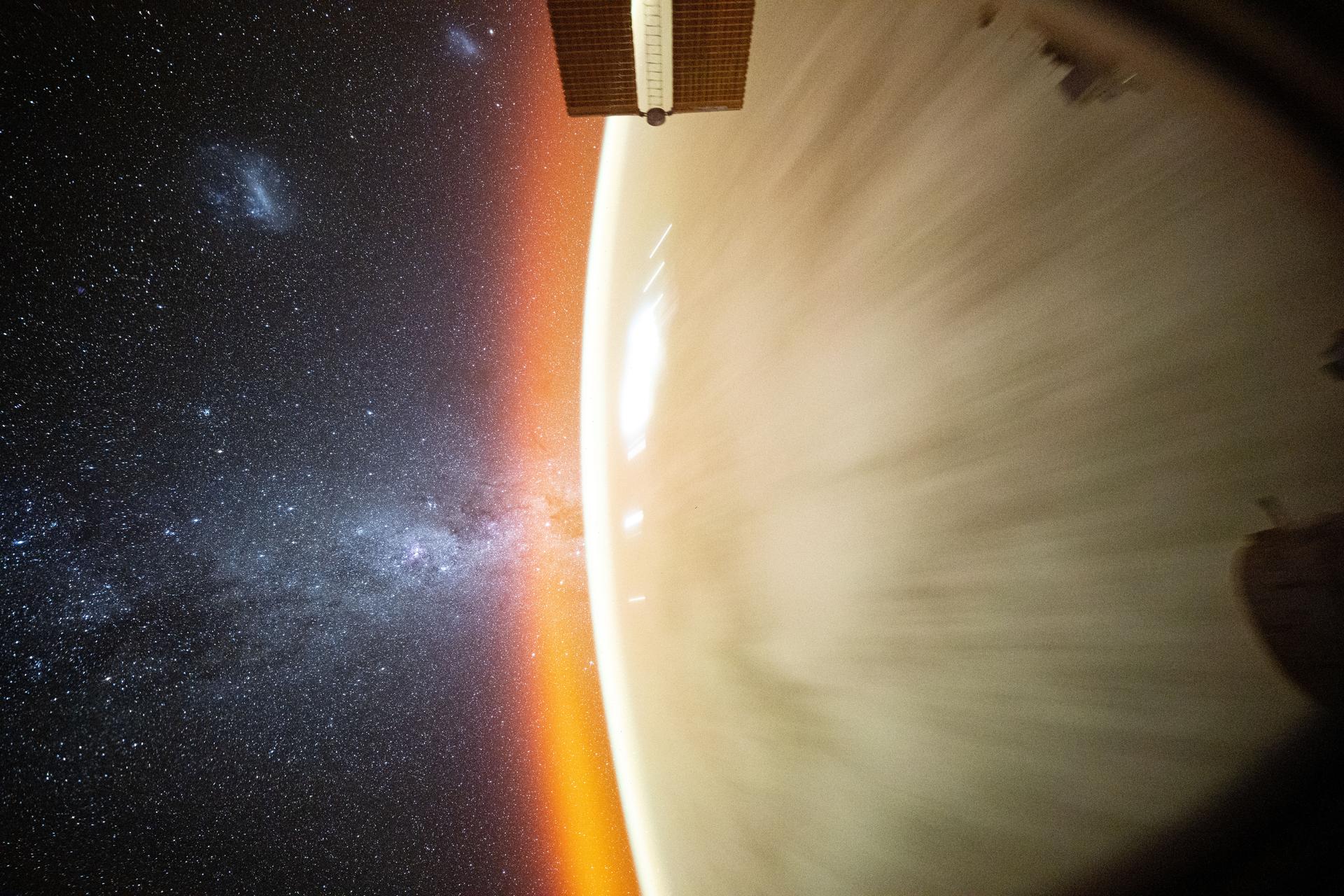 This celestial image captured by NASA astronaut Don Pettit using a camera with low light and long duration settings pointed out a window on the SpaceX Dragon crew spacecraft shows the Milky Way beyond Earth's horizon crowned by an atmospheric glow. The Large and Small Magellanic Clouds are also distinguishable as the International Space Station orbited 257 miles above the Pacific Ocean.