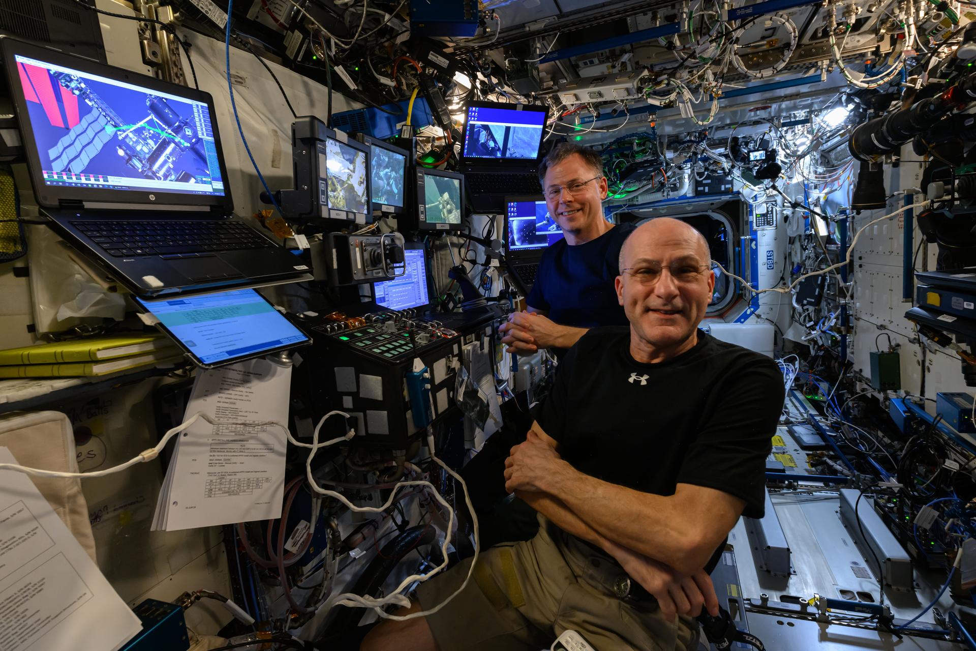 NASA astronauts Don Pettit (foreground) and Nick Hague, both Expedition 72 flight engineers, are at the controls of the robotics workstation preparing to assist and monitor spacewalkers Suni Williams and Butch Wilmore (not pictured). Williams and Wilmore worked outside the International Space Station during a five-hour and 26-minute spacewalk on Jan. 30, 2025, to remove radio communications hardware and swab external surfaces searching for potential microorganisms.