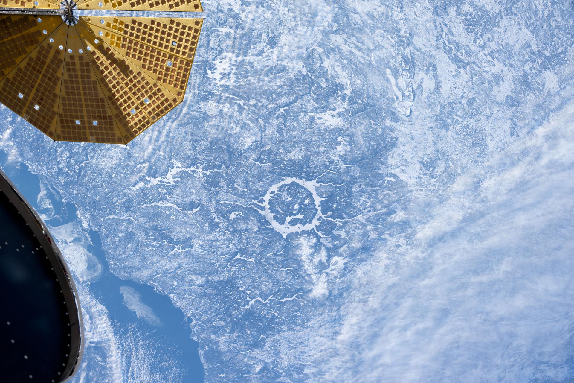 An UltraFex solar array, one of two cymbal-shaped solar arrays on the Northrop Grumman Cygnus space freighter, is pictured in the foreground as the International Space Station orbited 261 miles above the 214 million-year-old Manicouagan crater in Quebec, Canada.