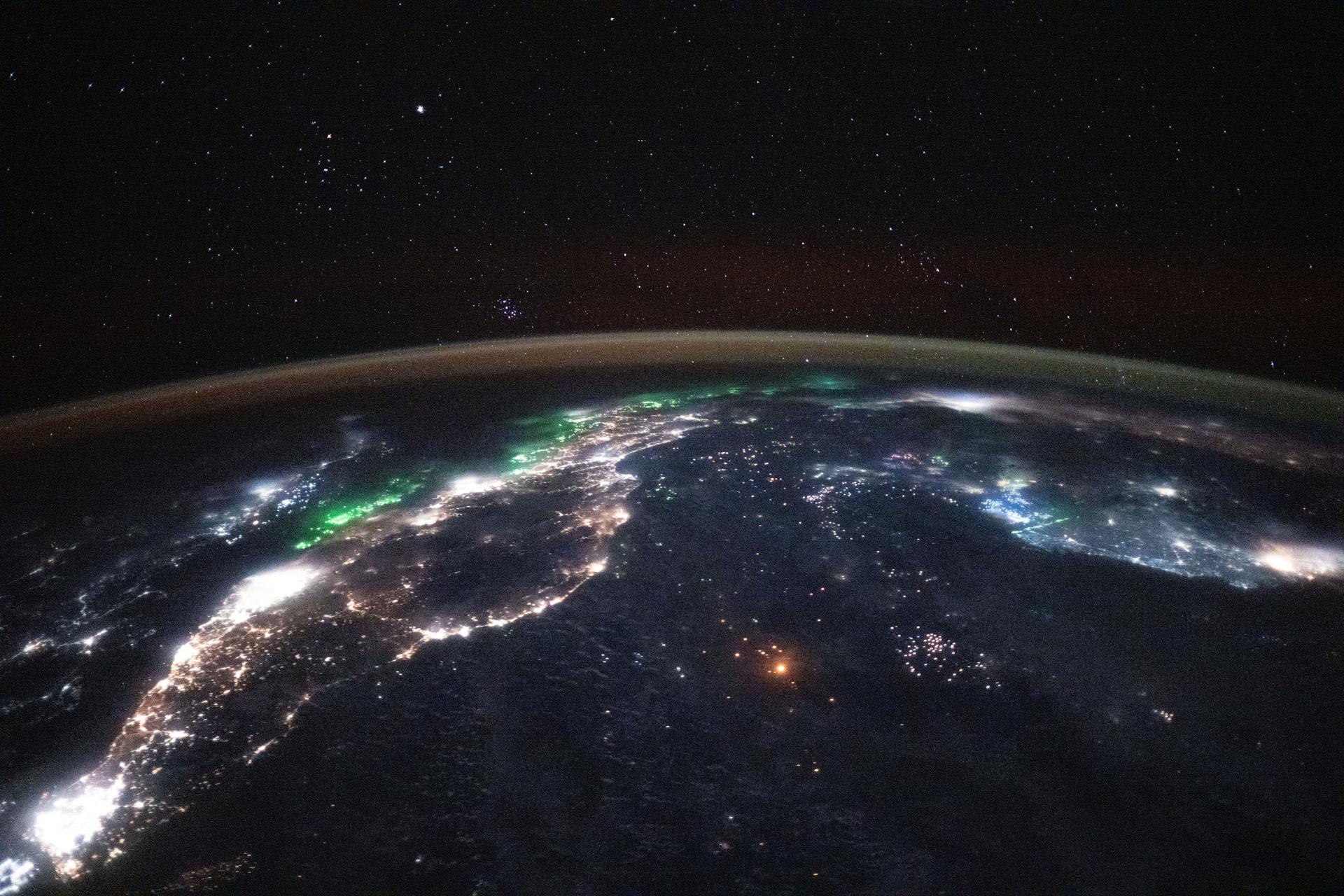 A starry night sky and an atmospheric glow blanket Earth's horizon in this photograph from the International Space Station orbiting 257 miles above Southeast Asia at 12:42 a.m. local time. Extending from bottom left, the brightest city lights are Singapore and Kuala Lumpur on the Malay Peninsula. At center, fishing boats and their lights dot the Gulf of Thailand and the South China Sea. At far right, is Ho Chi Minh City in Vietnam. Other major urban areas captured in this photograph include Phnom Penh, Cambodia, and Bangkok, Thailand.
