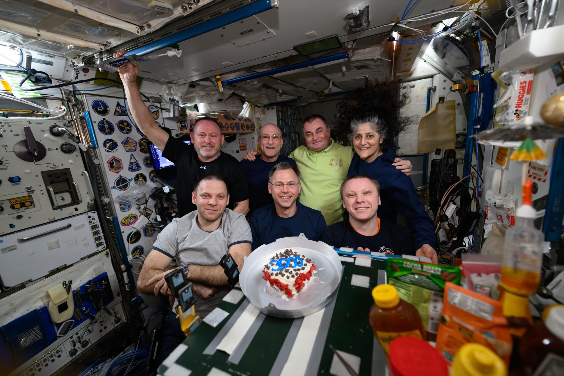 The Expedition 72 crew poses for a portrait inside the International Space Station's Harmony module with a cake commemorating a total of 3,000 cumulative days in space gained between the individual crew members. In the front row (from left), are Roscosmos cosmonaut Ivan vagner, NASA astronaut Nick Hague, and Roscosmos cosmonaut Aleksandr Gorbunov. In the back (from left), are NASA astronauts Butch Wilmore and Don Pettit, Roscosmos cosmonaut Alexey Ovchinin, and NASA astronaut Suni Williams.