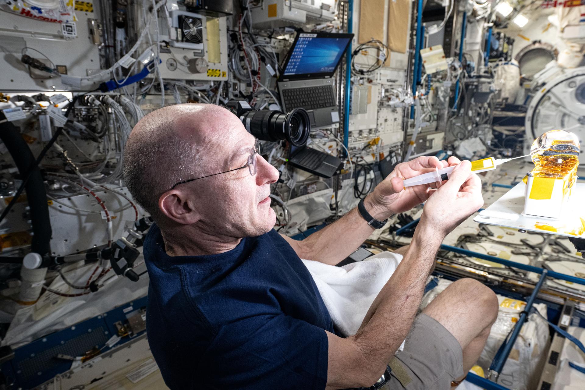 NASA astronaut and Expedition 72 Flight Engineer Don Pettit injects yellow ink into a ball of water shaped by microgravity and attached to research hardware by surface tension. Pettit was demonstrating simple space physics phenomena inside the International Space Station's Kibo laboratory module.