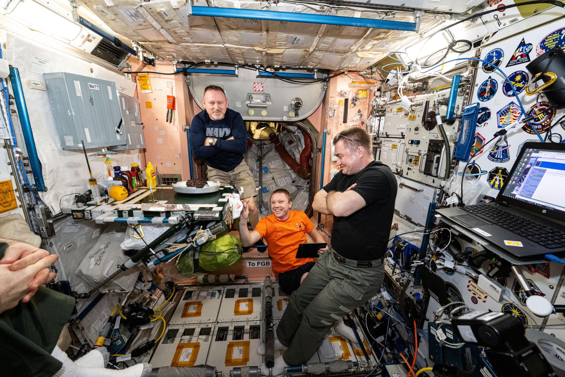 (From left) NASA astronaut Butch Wilmore and Roscosmos cosmonaut Aleksandr Gorbunov, both Expedition 72 flight engineers, and International Space Station Commander Alexey Ovchinin from Roscosmos join each other for dessert inside the Unity module's galley aboard the International Space Station.