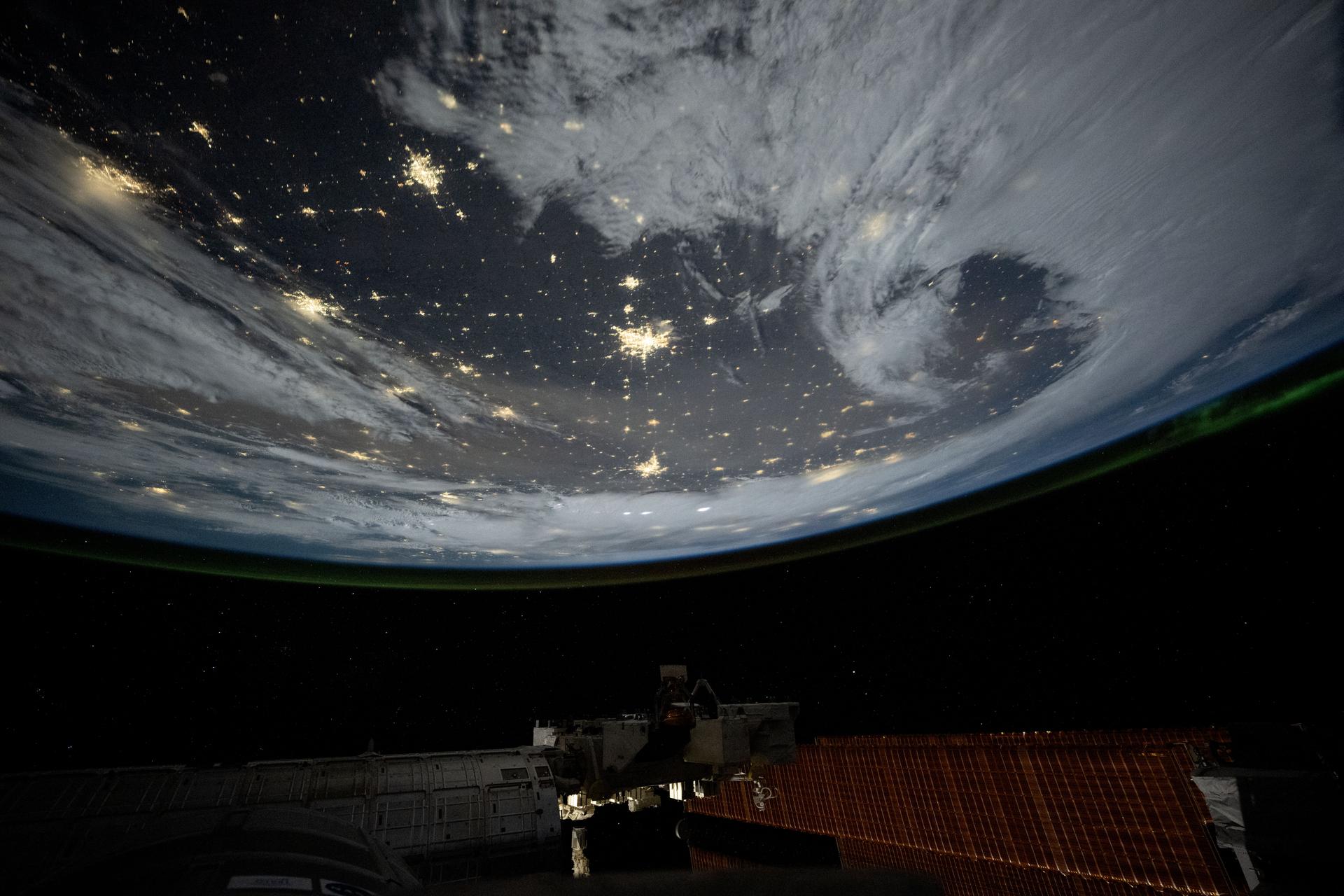 City lights dot the cloudy, midwestern landscape of the United States with a wispy aurora above Earth's horizon in this photograph from the International Space Station as it orbited 261 miles above the Sunflower State of Kansas. In the bottom foreground, is the Kibo laboratory module's Exposed Facility, an external research platform, and the orbital outpost's main solar arrays.