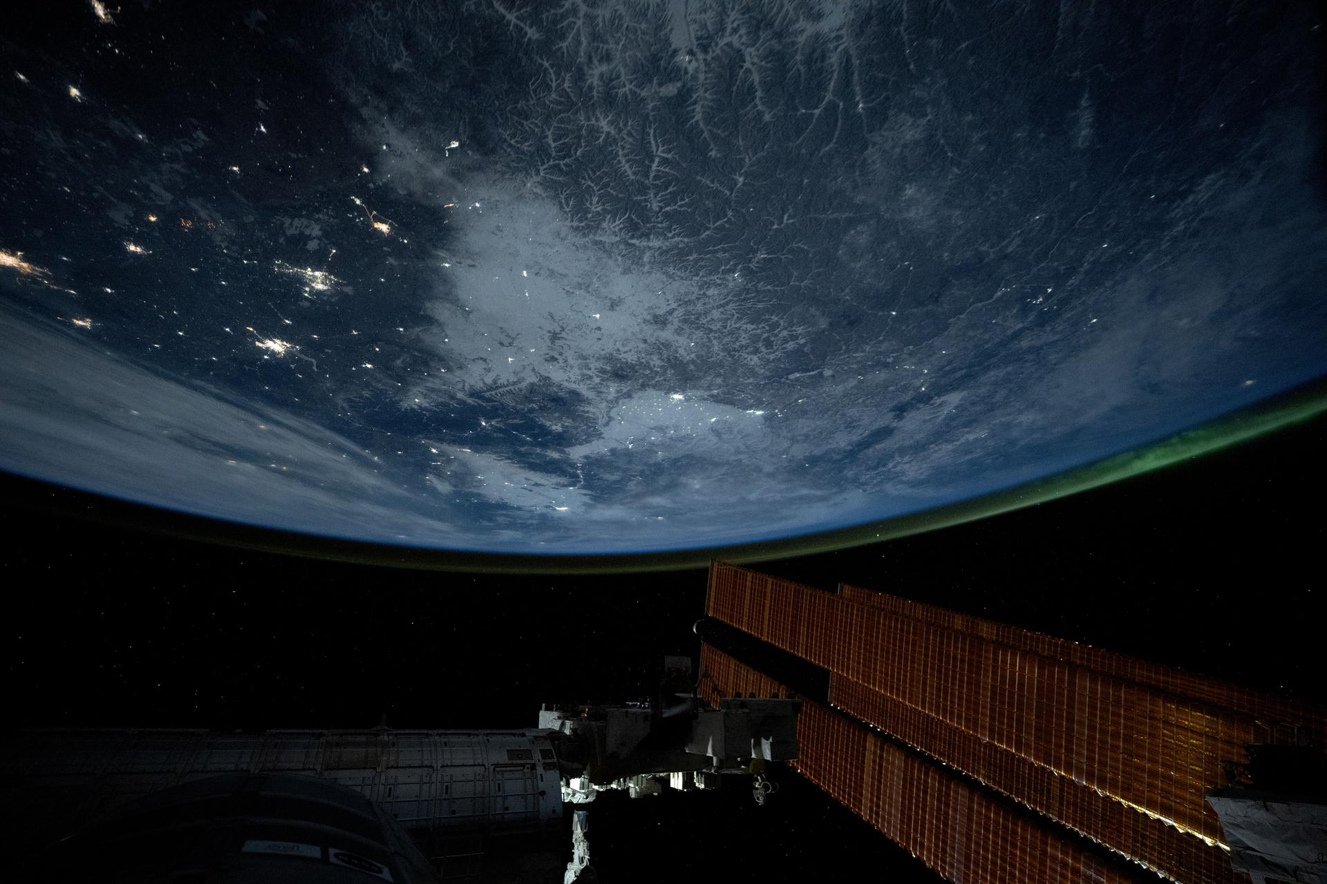 City lights dot the northeastern landscape of China with a wispy aurora above Earth's horizon in this photograph from the International Space Station as it orbited 262 miles above Asia. In the bottom foreground, is the Kibo laboratory module's Exposed Facility, an external research platform, and the orbital outpost's main solar arrays.