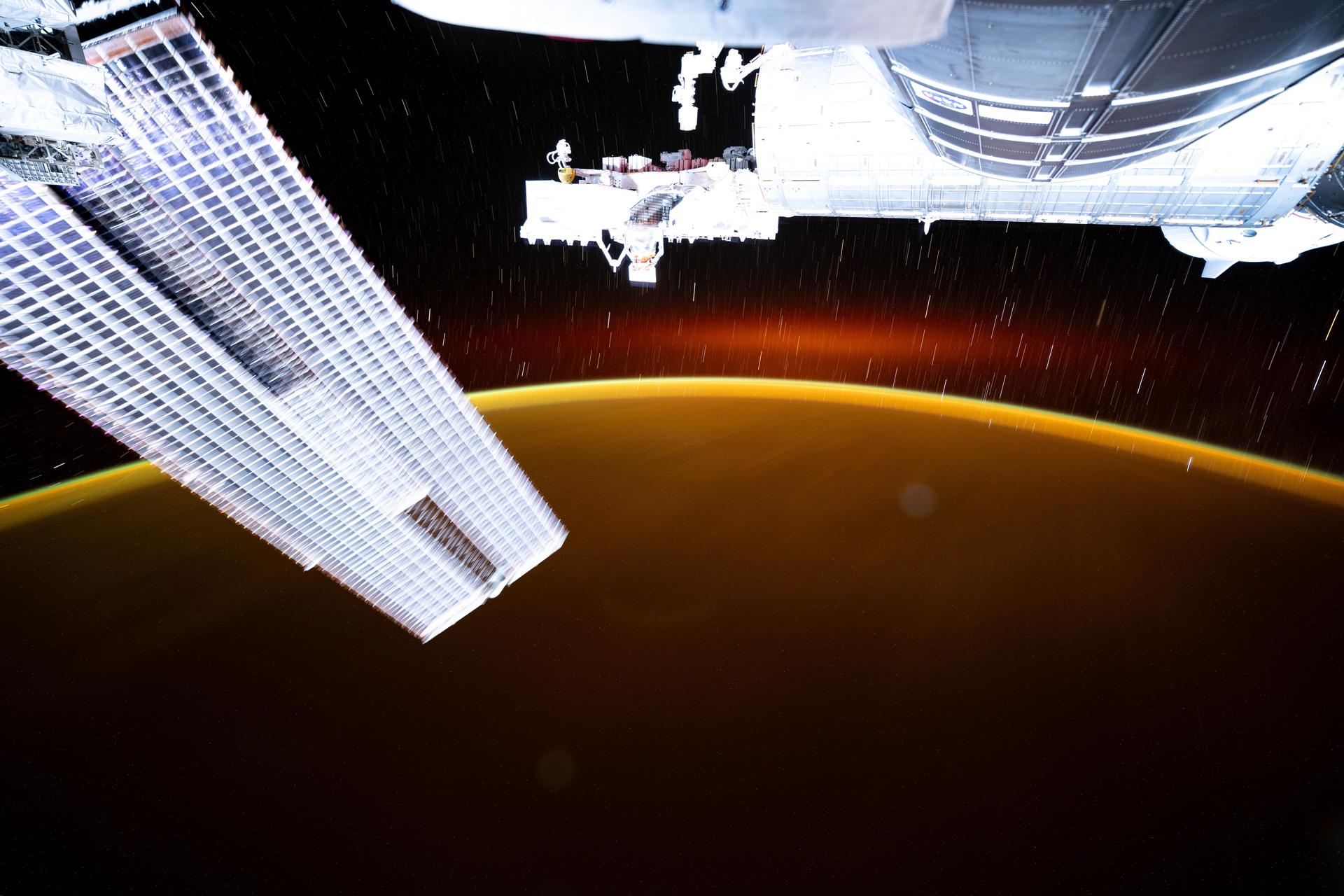 This long-duration photograph from the International Space Station highlights star trails and an atmospheric glow blanketing Earth's horizon. In the foreground, is a set of the space station's main solar arrays (left), the Kibo laboratory module (right), and Kibo's External Platform that houses experiments exposed to the vacuum of space. The orbital outpost was soaring 259 miles above the Pacific Ocean southeast of Japan moments before sunset.